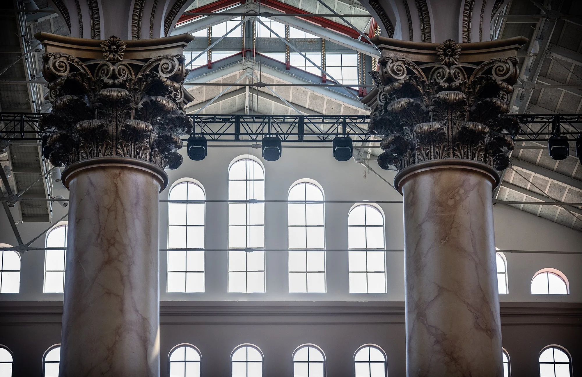Interior of a building with large marble columns, arched windows, and decorative arches, possibly a historical or government building, with scaffolding and lighting fixtures visible.