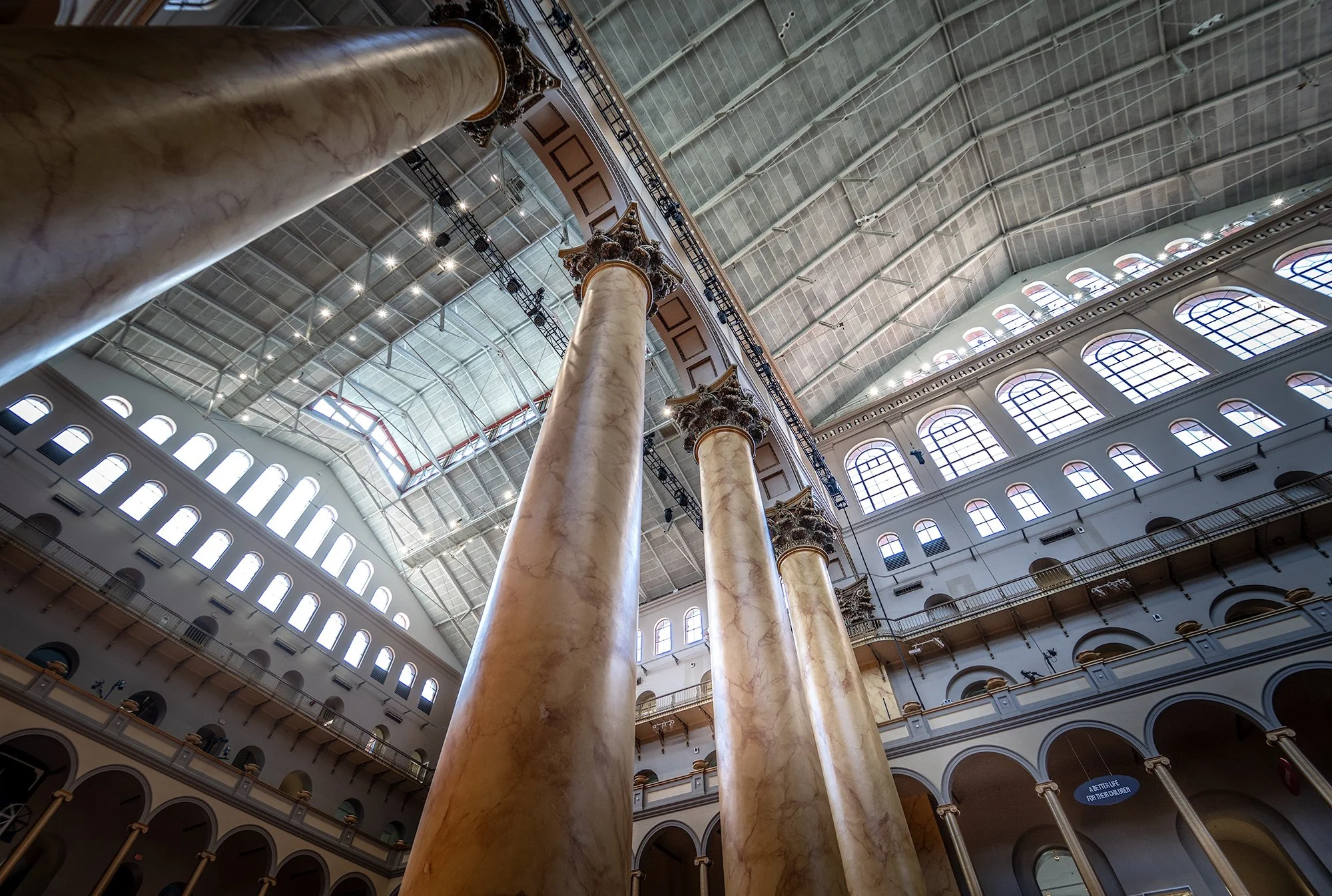 Interior of a grand historic building with large marble columns supporting a high, arched ceiling with numerous windows, railings, and lighting.