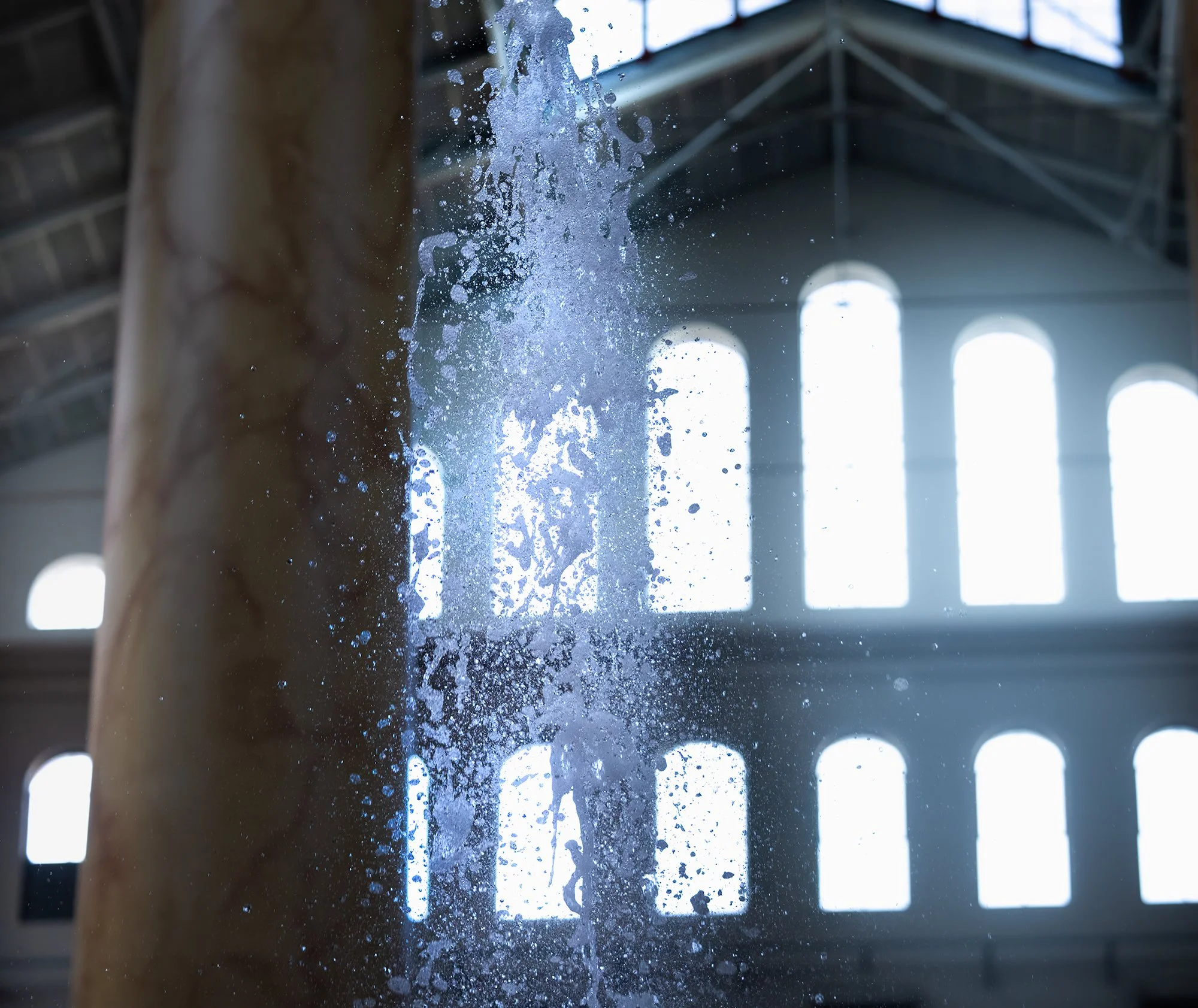 Water splashing or dripping from a building or structure inside a large industrial-style space with high ceilings and large windows.