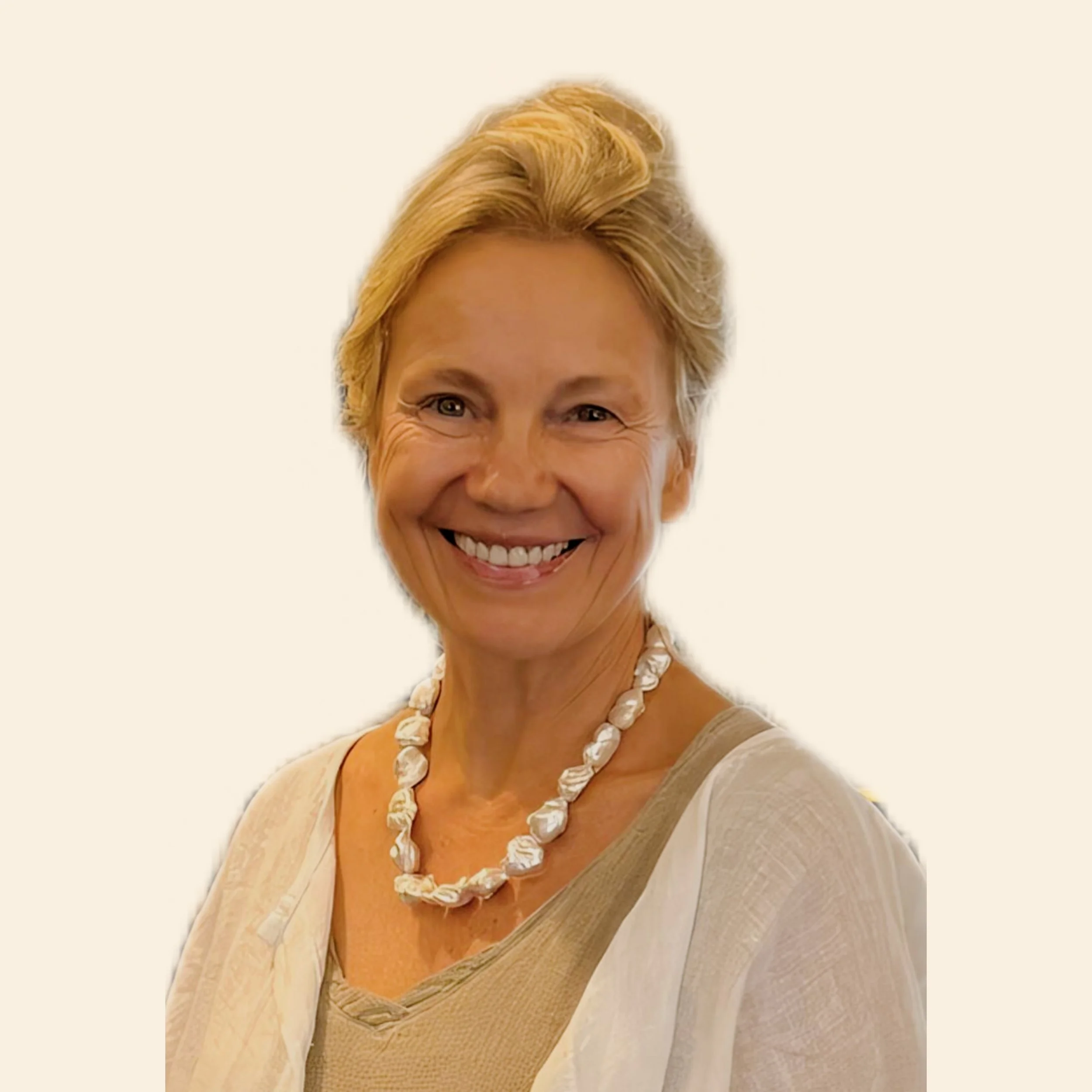 Close-up of a woman with short blonde hair, wearing a pearl necklace and beige top, smiling.