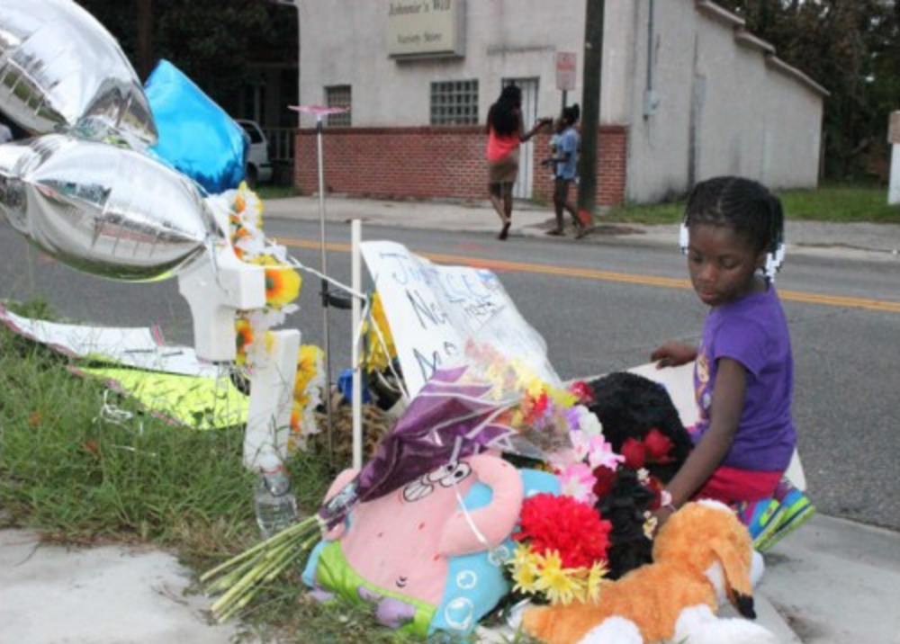  Nyasia Lewis, 6, kneels to add a sign to a roadside memorial for 29-year-old Charles Smith, who was shot and killed by Savannah-Chatham police after breaking free from a patrol car in September 2014. &nbsp;(Dash Coleman/Savannah Morning News)&nbsp; 