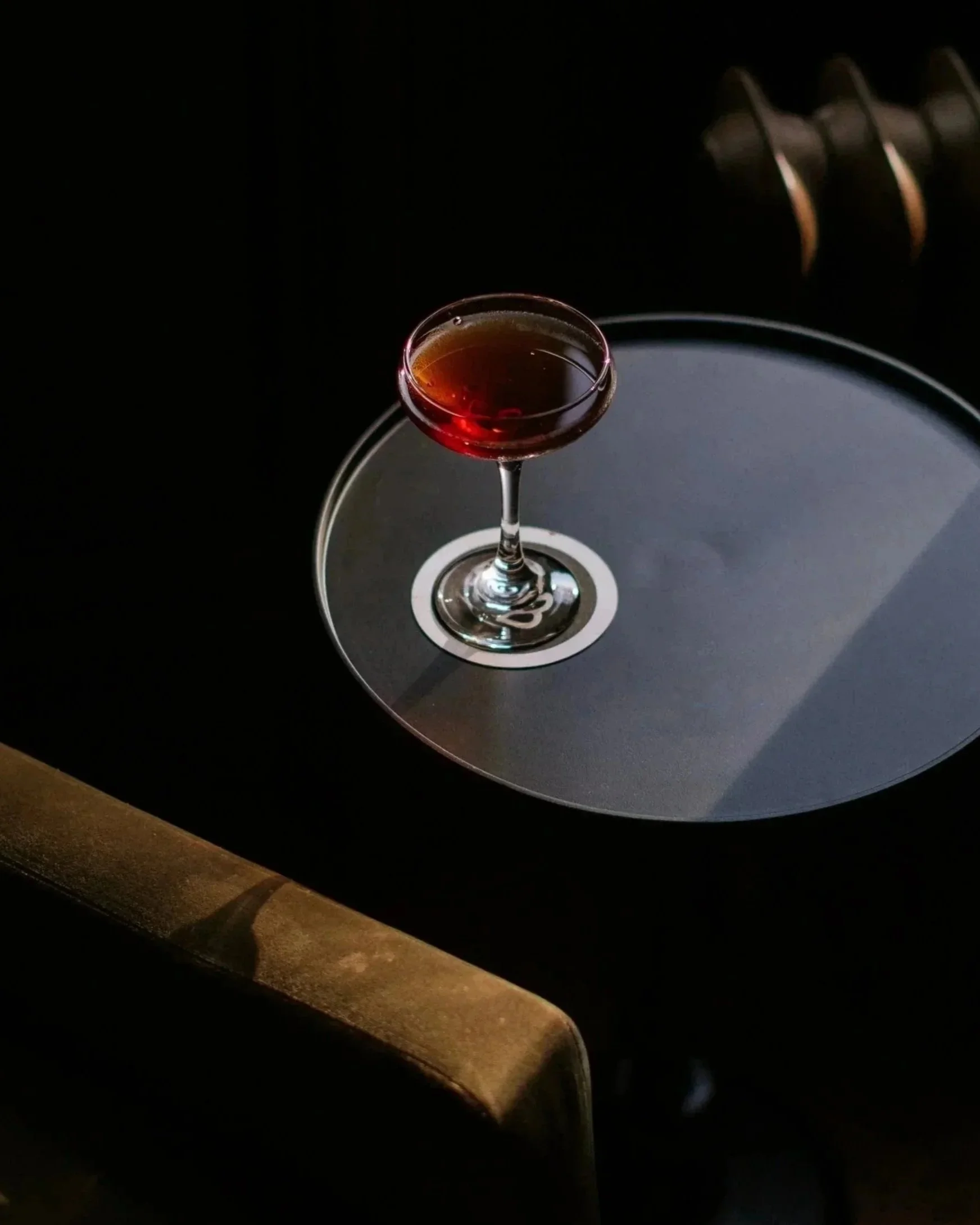 A glass of red wine on a small round table with black top, in a dimly lit setting.