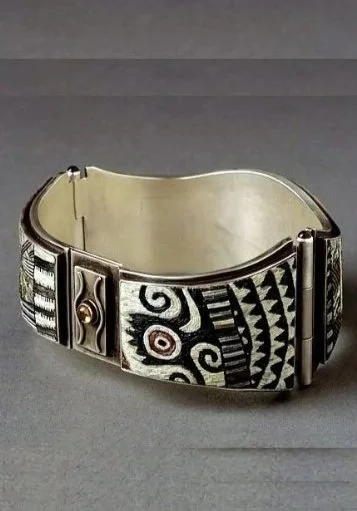A silver cuff bracelet with black and white tribal or geometric patterns and designs.