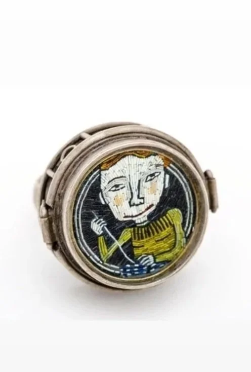 A round watch with an embroidered face featuring a cartoon-style person with light skin and short hair, holding a stick or wand, wearing a yellow and black striped shirt, against a black background.