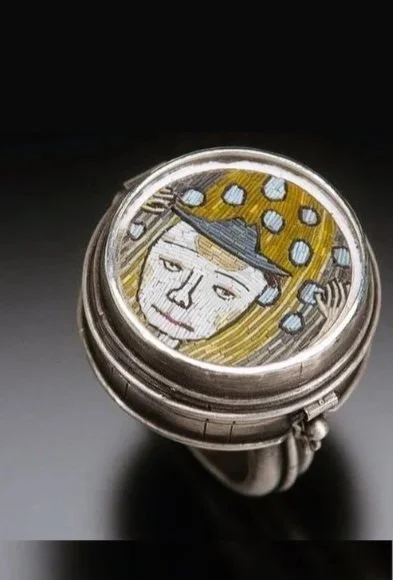 A close-up of a ring with a design of a man's face, wearing a hat and holding a sword, depicted in a comic style.