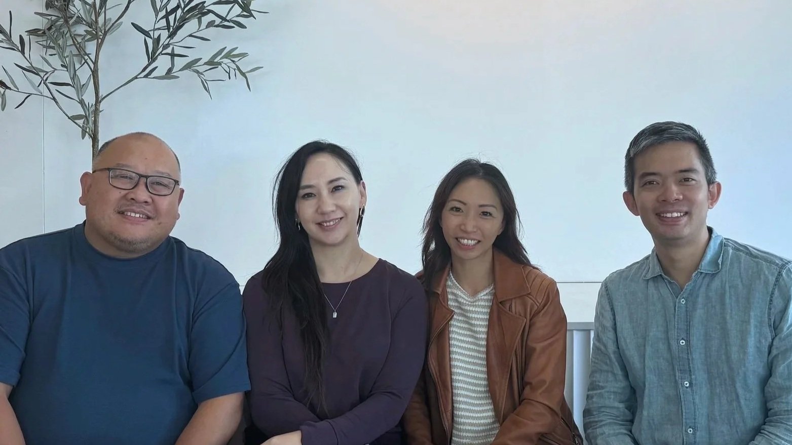 A woman and a man sitting together at a table, smiling at the camera in a bright indoor setting.