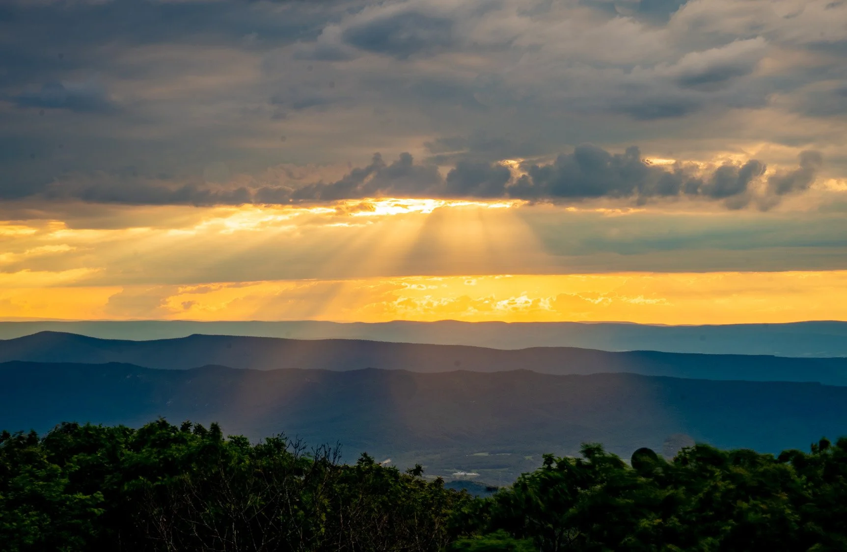 Golden hour sunlight rays breaking through clouds over layered mountains in Shenandoah National Park