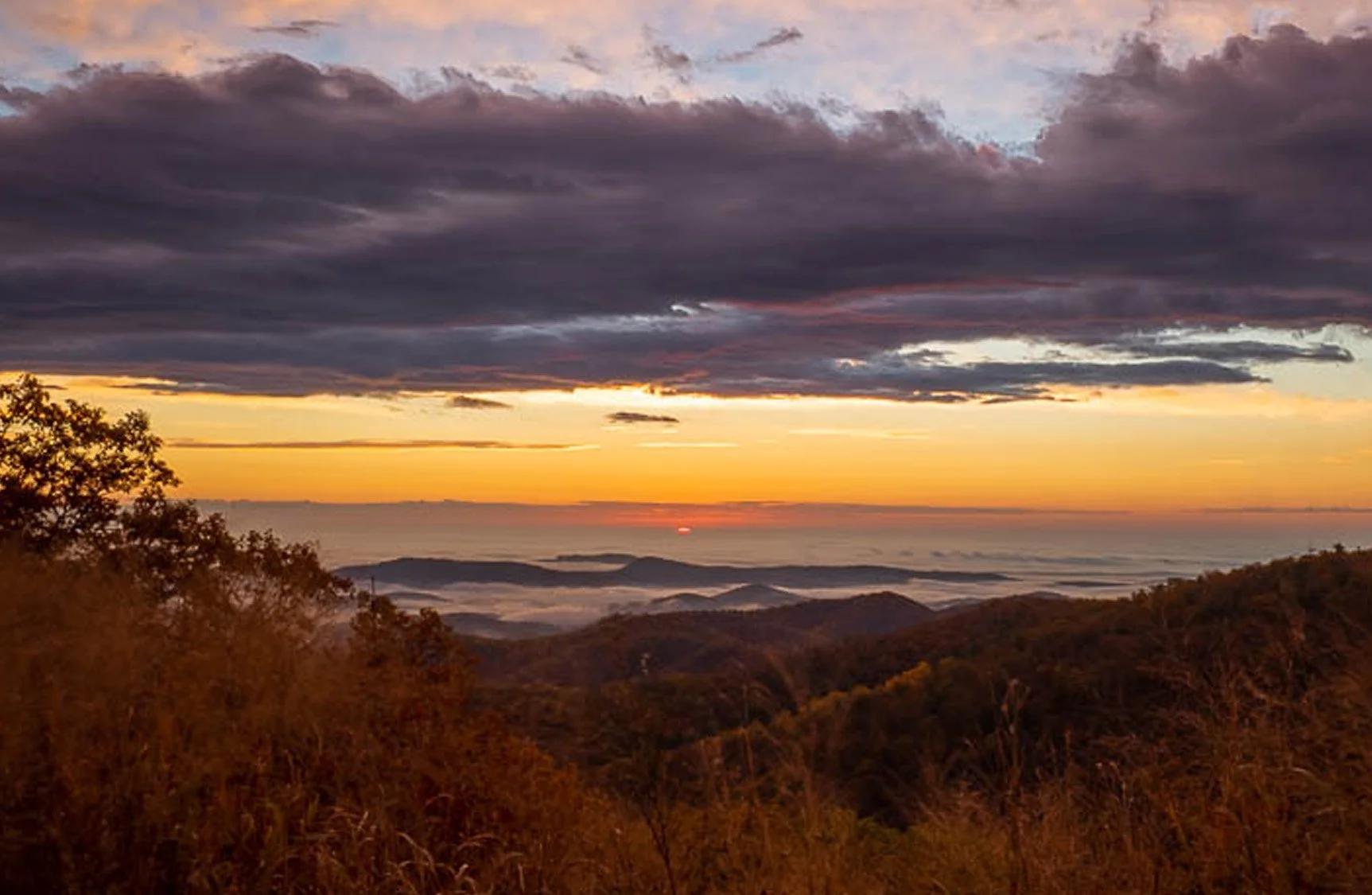 Sunrise over rolling hills and valleys from Jenkins Gap Overlook in Shenandoah National Park, with soft golden light and layered mountain views facing east toward the Piedmont.