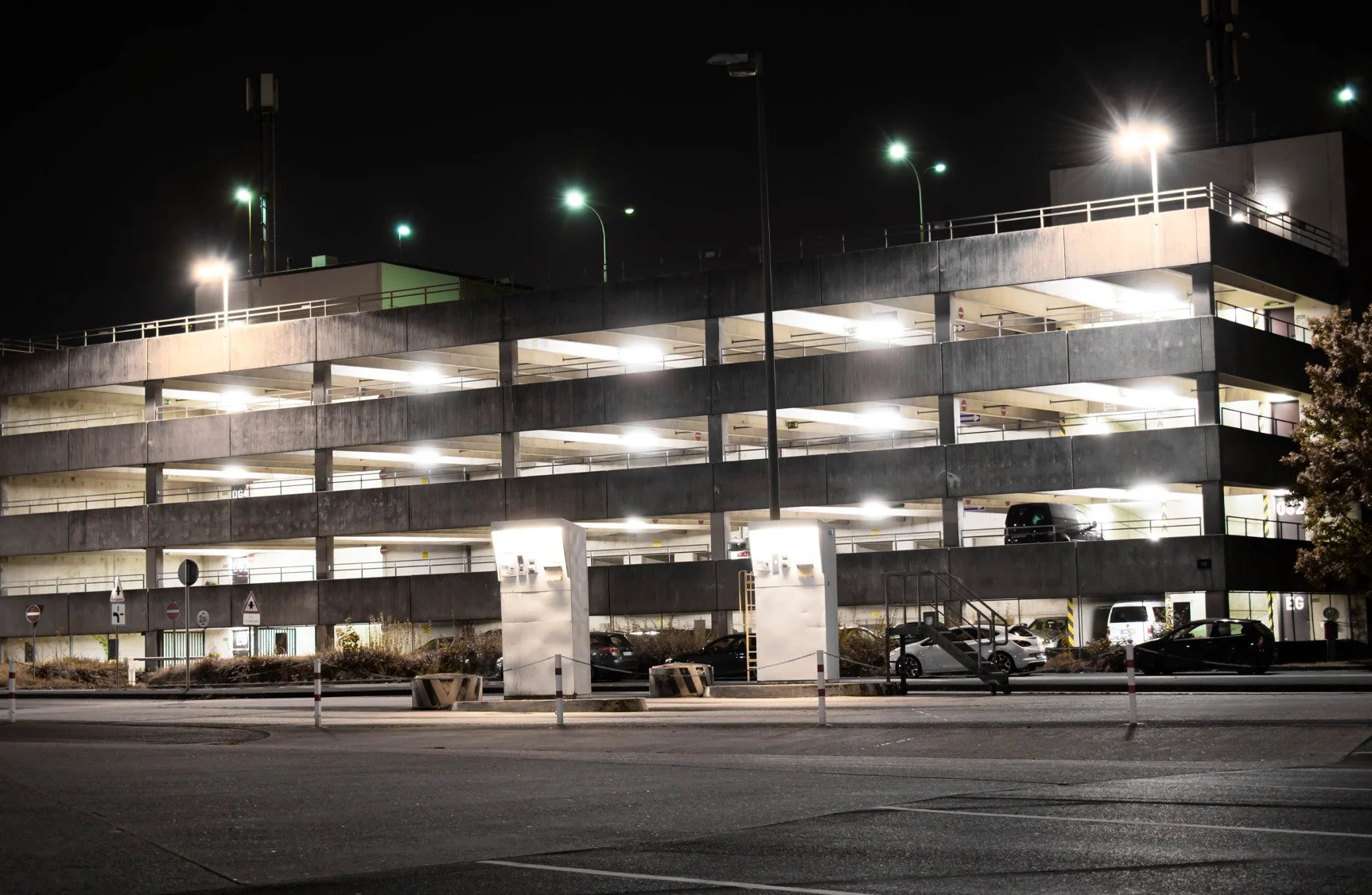 Nighttime view of a multi-level parking garage with cars parked inside, illuminated by bright lights along a city street.
