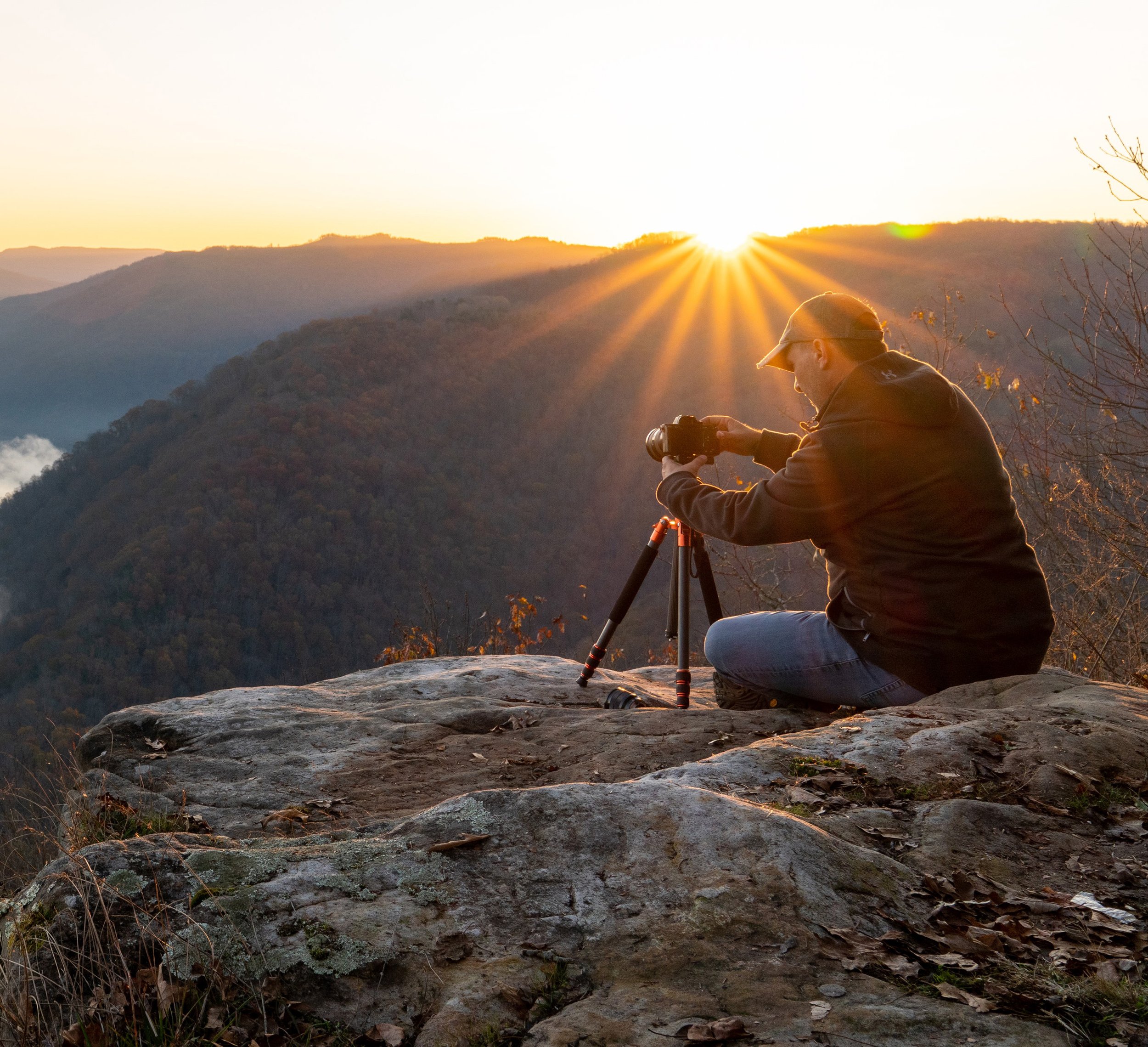 Photographer setting up tripod at sunrise during outdoor mountain workshop.