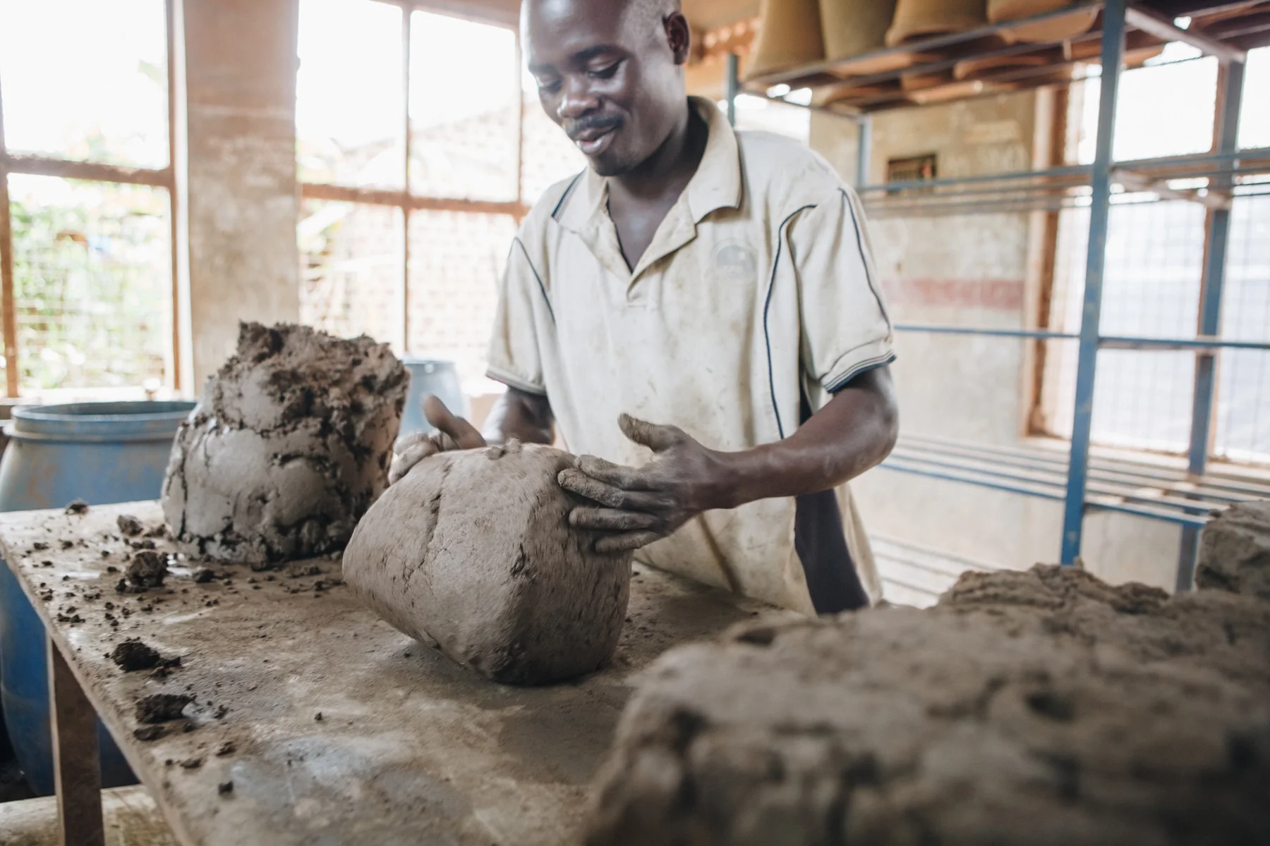 ©TomWoollard_Yunus-Social-Business_Uganda_Spoutsofwater-african-man-hand-moulding-clay-fllters-workshop.jpg