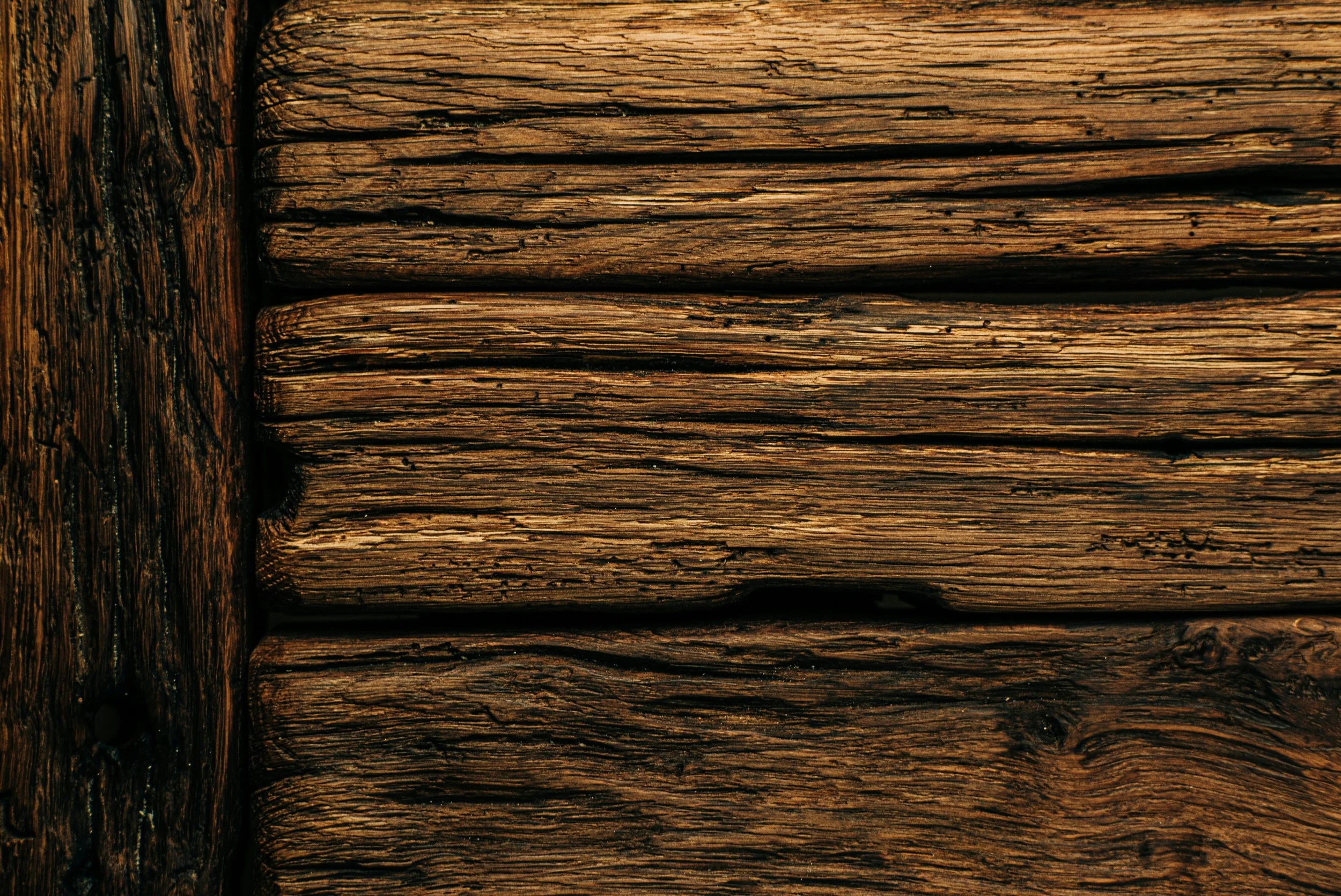 Close-up of weathered wooden planks with visible grain and cracks, arranged horizontally.
