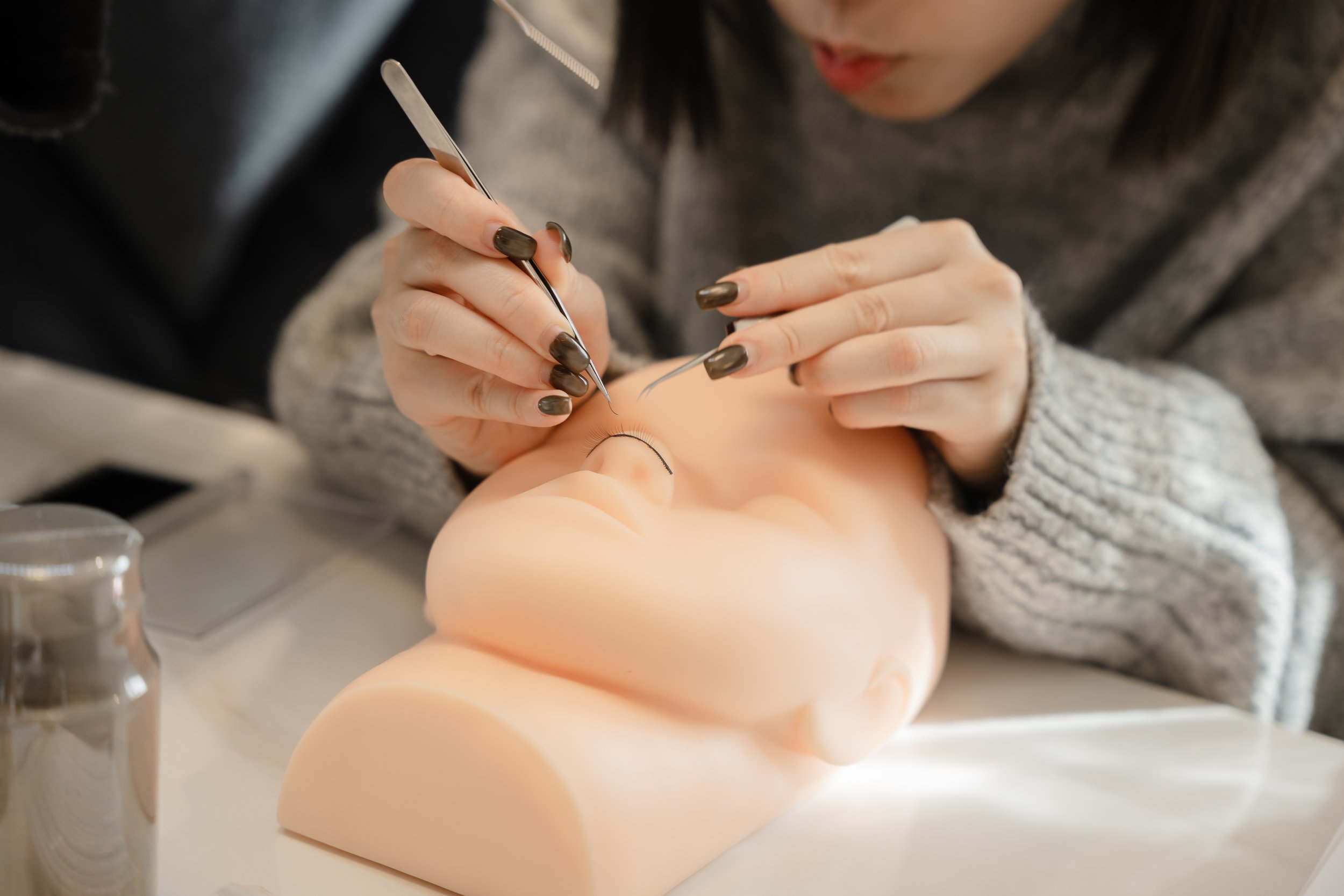 Person practicing eyelash extension application on mannequin head.