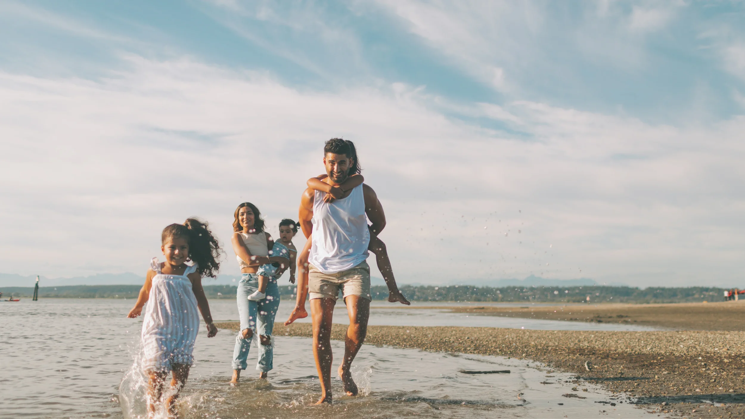 A happy family with children playing joyfully on a beach near the water during daytime with a cloudy sky.
