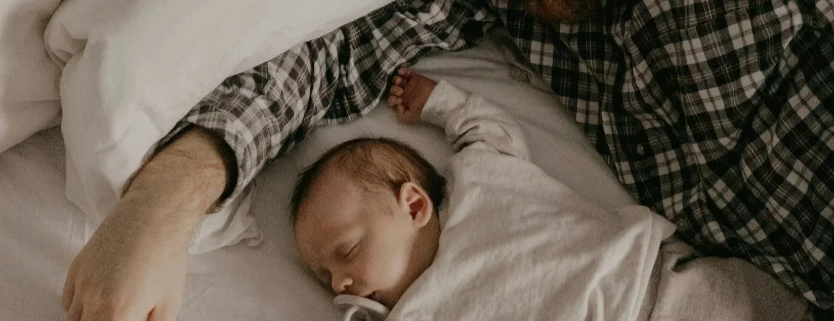 New born sleeping with tired new dad on the bed