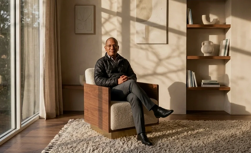 Psychologist Eric Brunet sitting in an arm chair of a naturally lit and neutrally furnished office space, Large window to the left with linen curtains