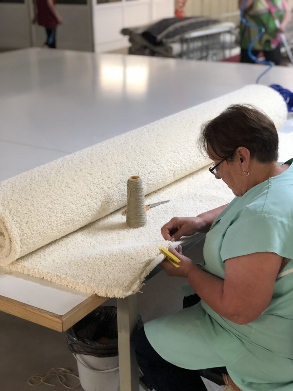 Rug being finished by hand with a triple-stitched textile border