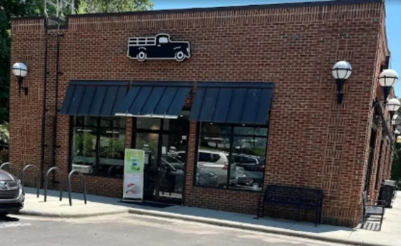 A brick building with large windows, black awnings, and a vintage truck sign above the entrance.