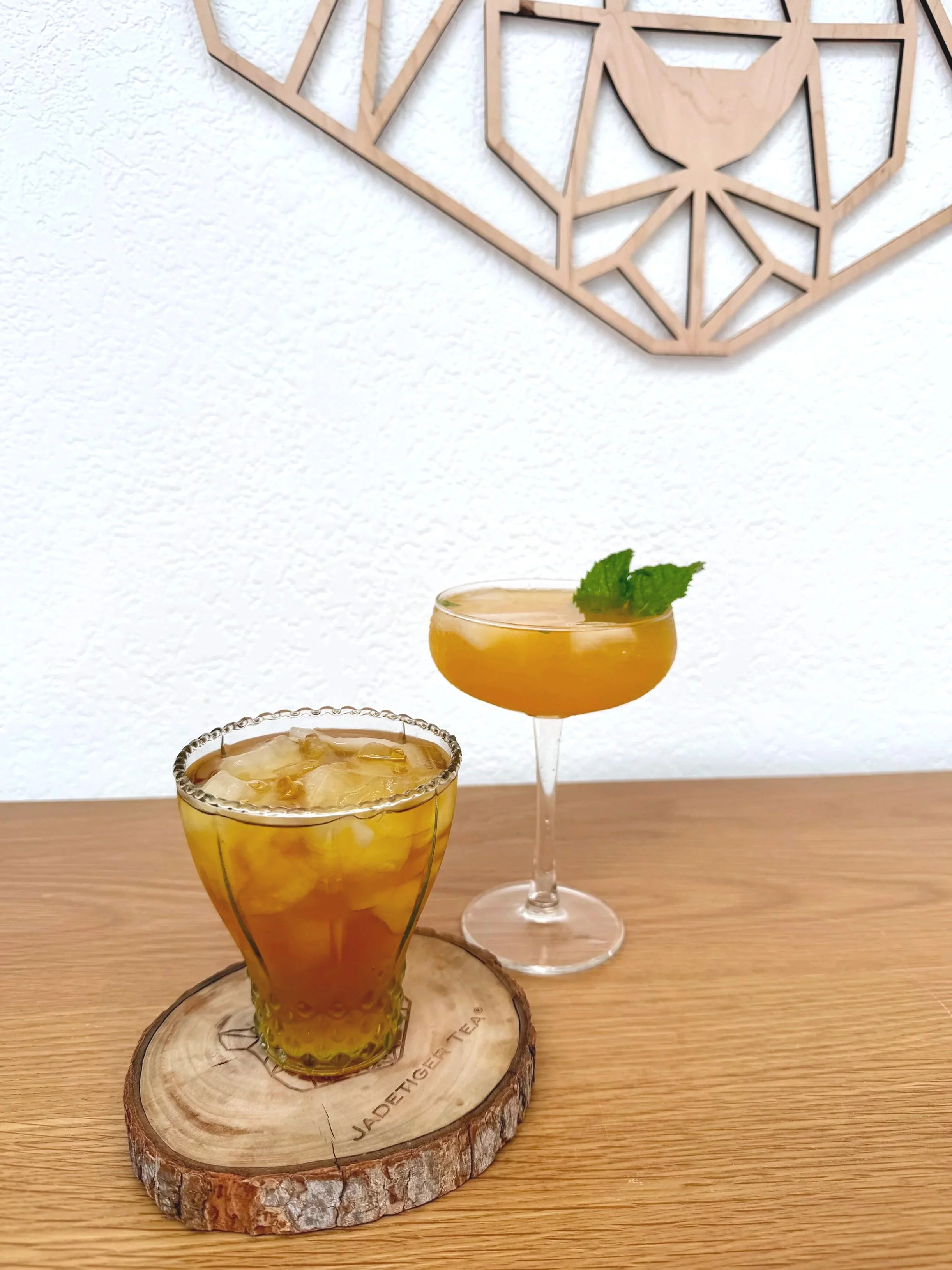 Mangocha™ green iced tea mocktail with mango puree, muddled mint and simple syrup. Served in 2 unique iced tea glasses with a mint leaf garnish.