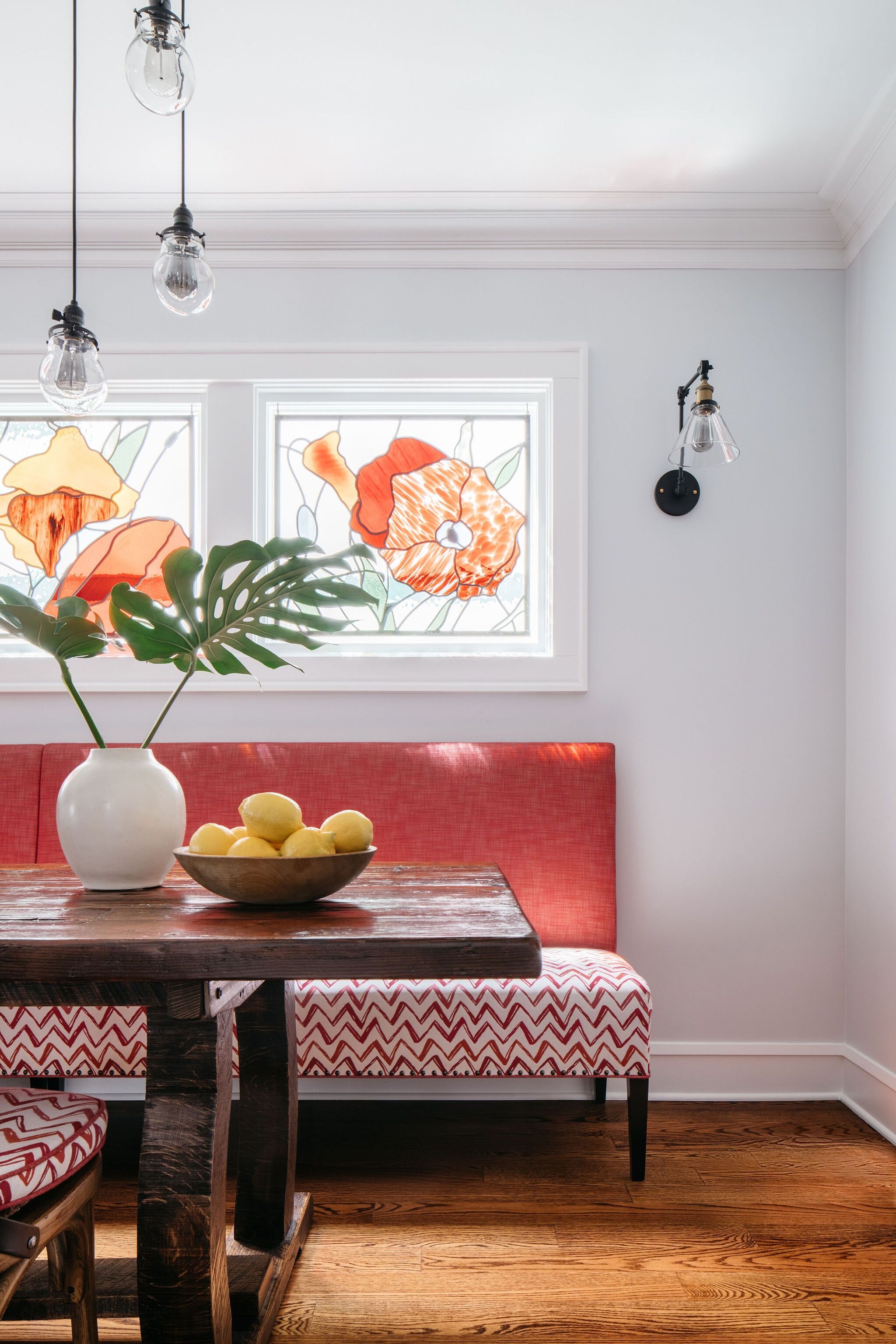 A custom banquette upholstered in a coral and red and white zig zag pattern with a custom walnut trestle table, bronze wall lights and modern ceiling three light pendants