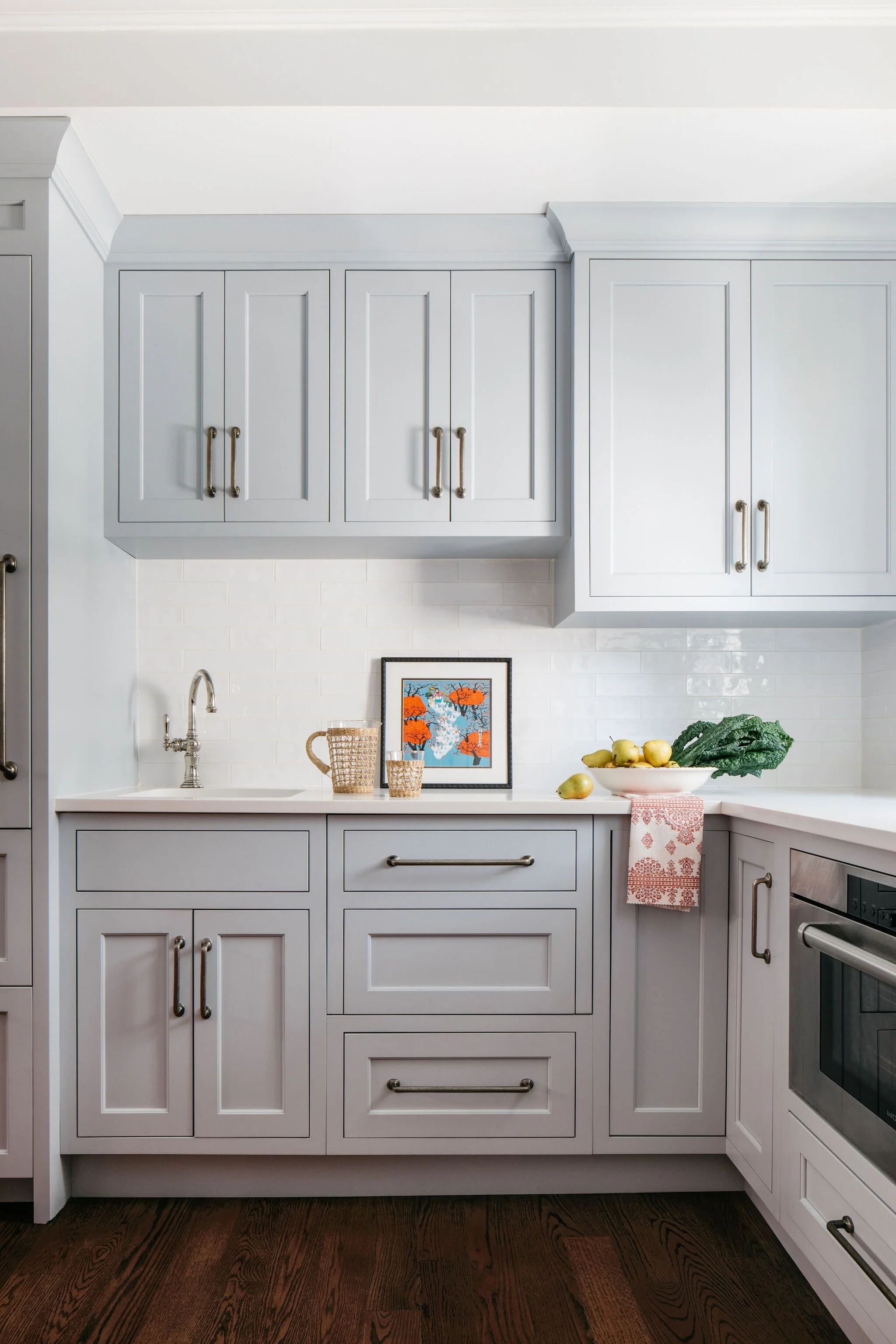 A pale blue kitchen with custom flush inset cabinets, iron pulls, white tile backsplash, bar sink and wicker accents