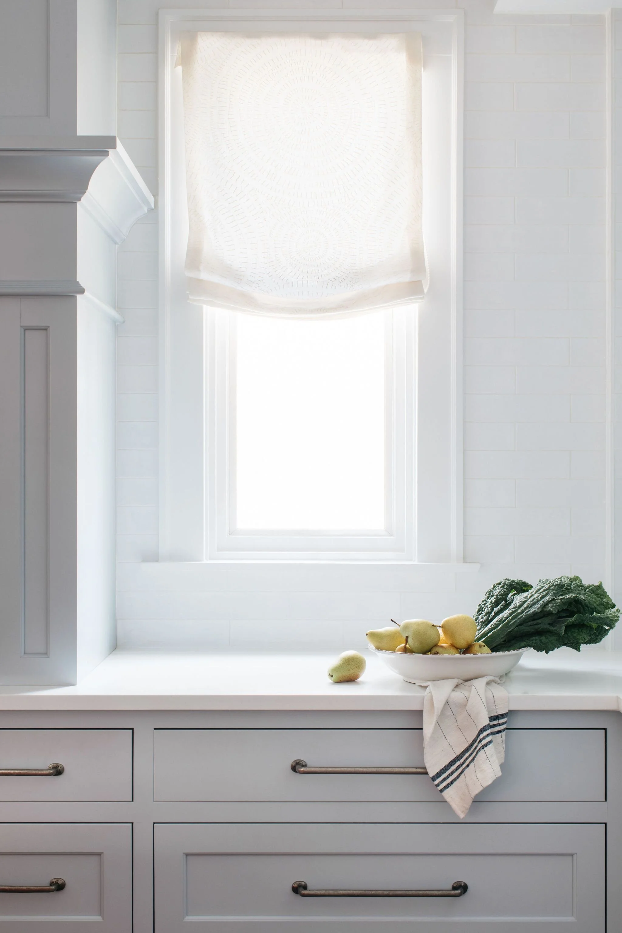 A moody kitchen vignette with pale blue custom cabinets, pewter iron pulls and an embroidered cream relaxed roman shade