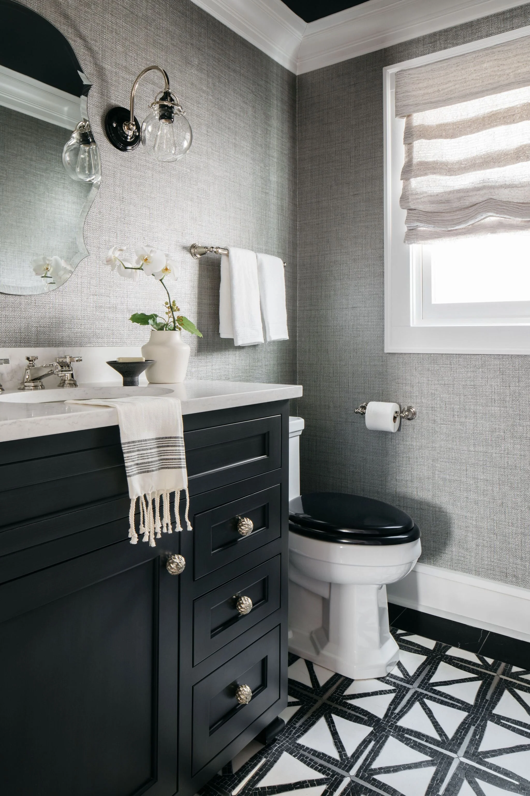 A modern Powder Room with New Ravenna mosaic marble floor with polished nickel inserts, black lacquer custom vanity, grasscloth wallpaper, wood toilet seat, and linen roman shade