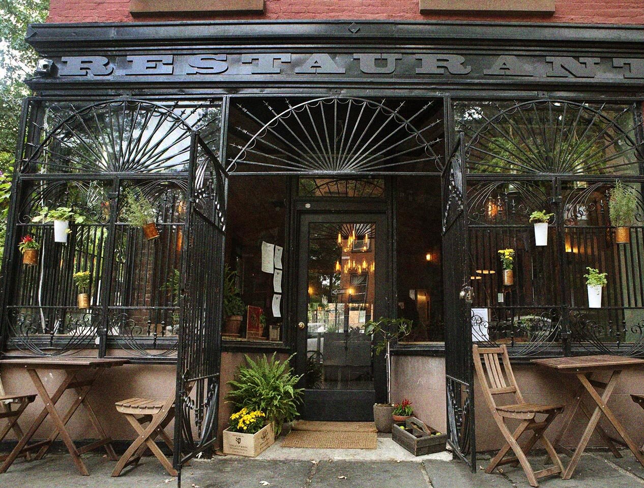 View of Rucola Restaurant from the street during the day. Two outdoor tables line the sidewalk.