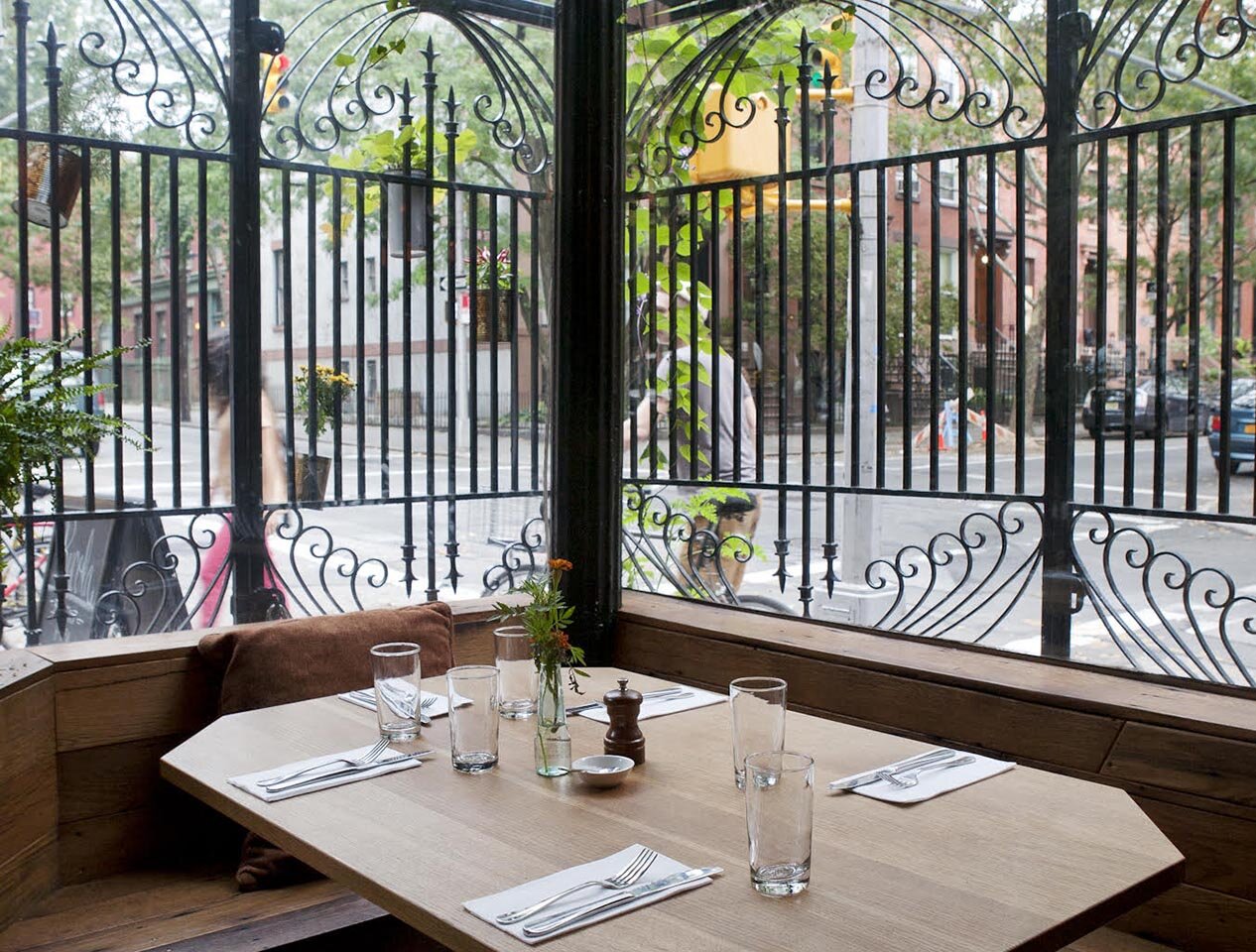 An empty corner table at Rucola during the day, with a view of the Brooklyn street outside the ornate window. 