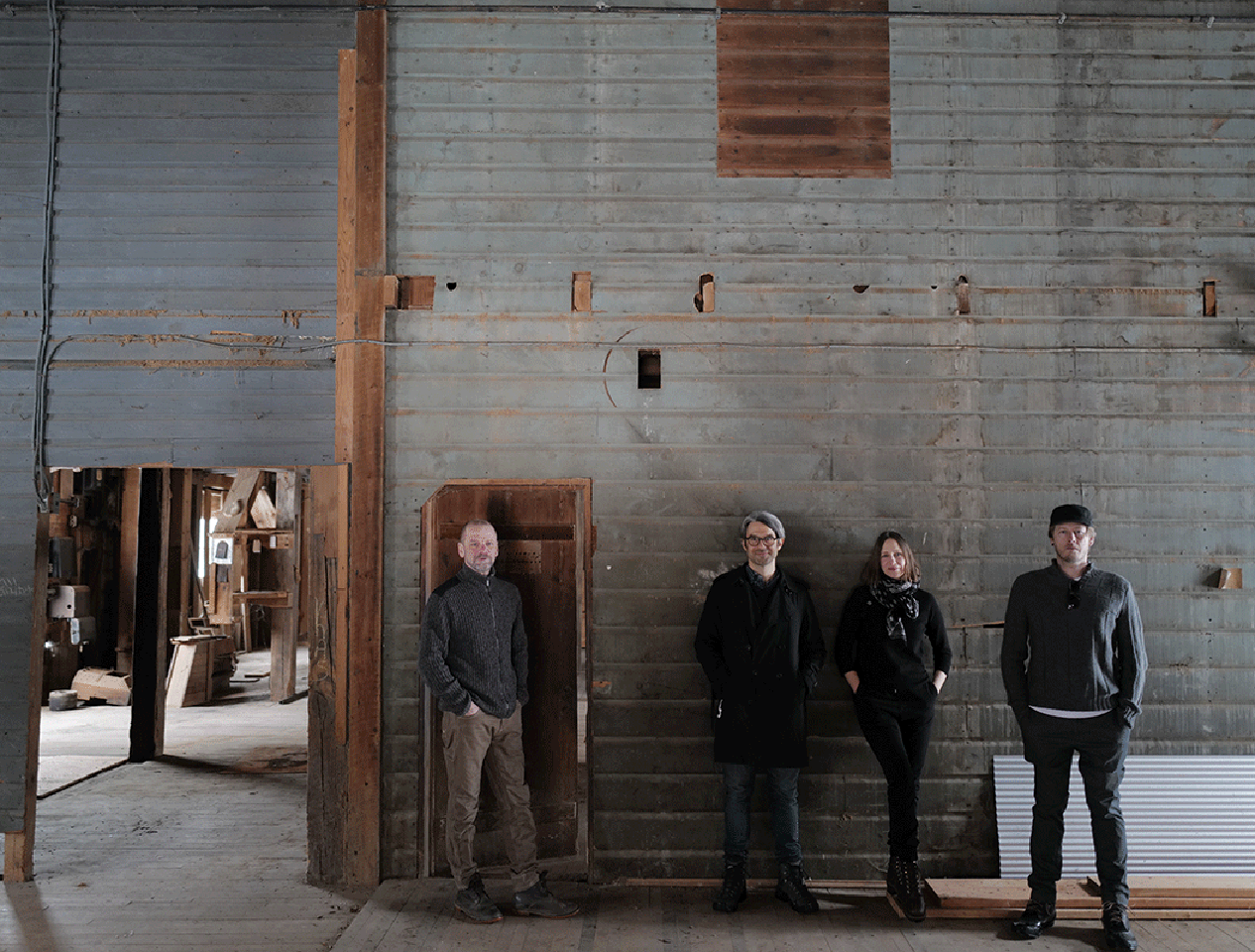 The Oberon Group does a site visit at the future site of The Granary in Accord, New York. Four people stand in front of an interior wall, with light streaming in from the right.