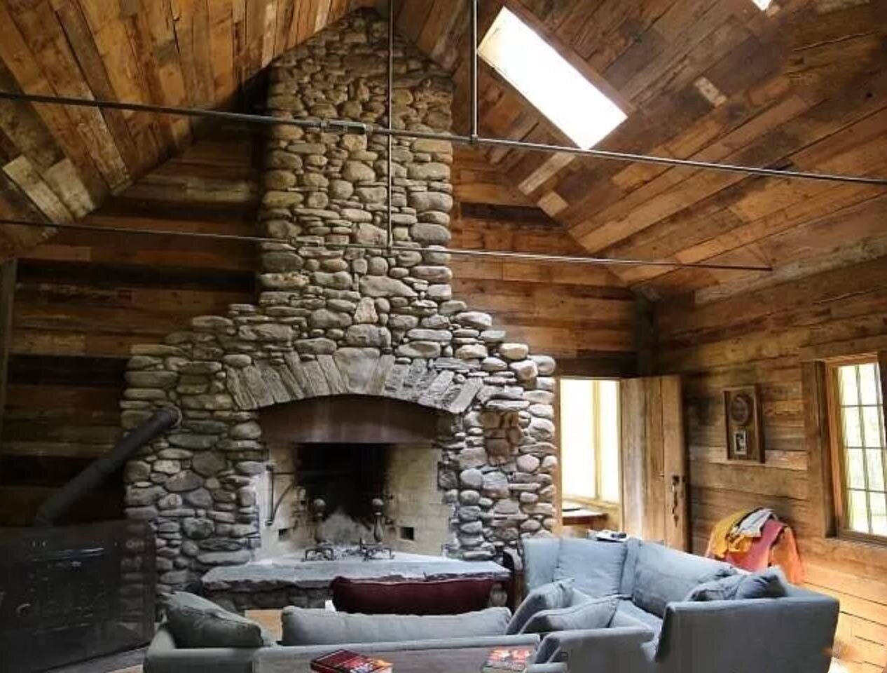 Interior of a building at Jenny Brook, with a large handmade stone fireplace and seating area underneath a vaulted ceiling.