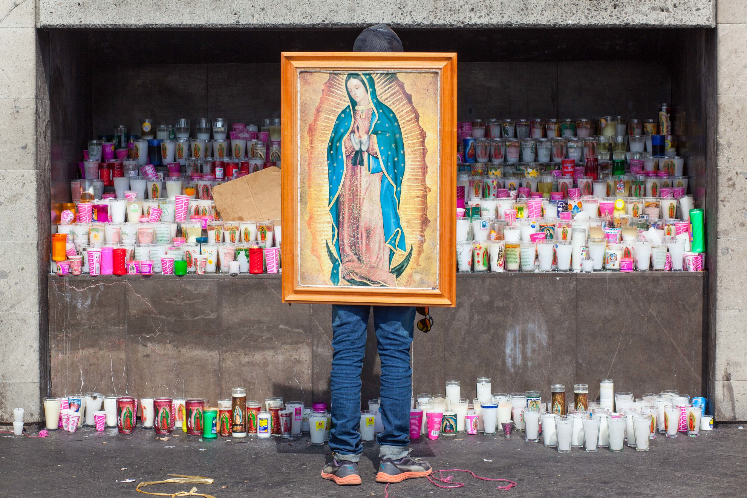 The Pilgrimage to the Basilica of Our Lady of Guadalupe, Mexico City, a man prays against a huge offering of candles. 