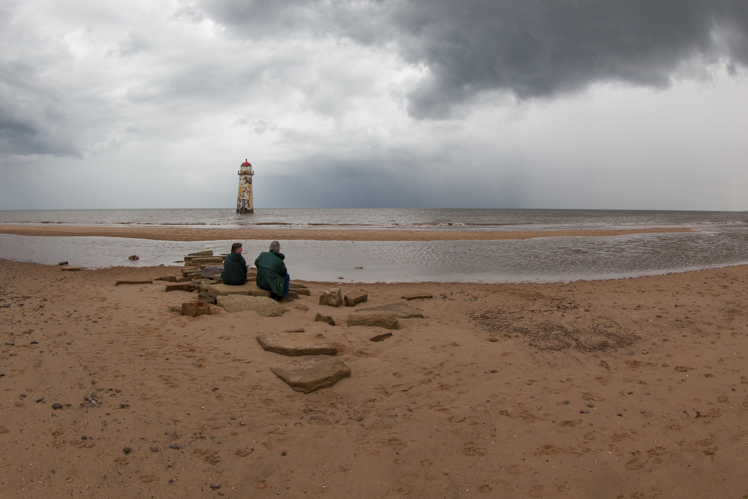 A couple sit on the beach in North Wales in front of the Talacre Lighthouse.