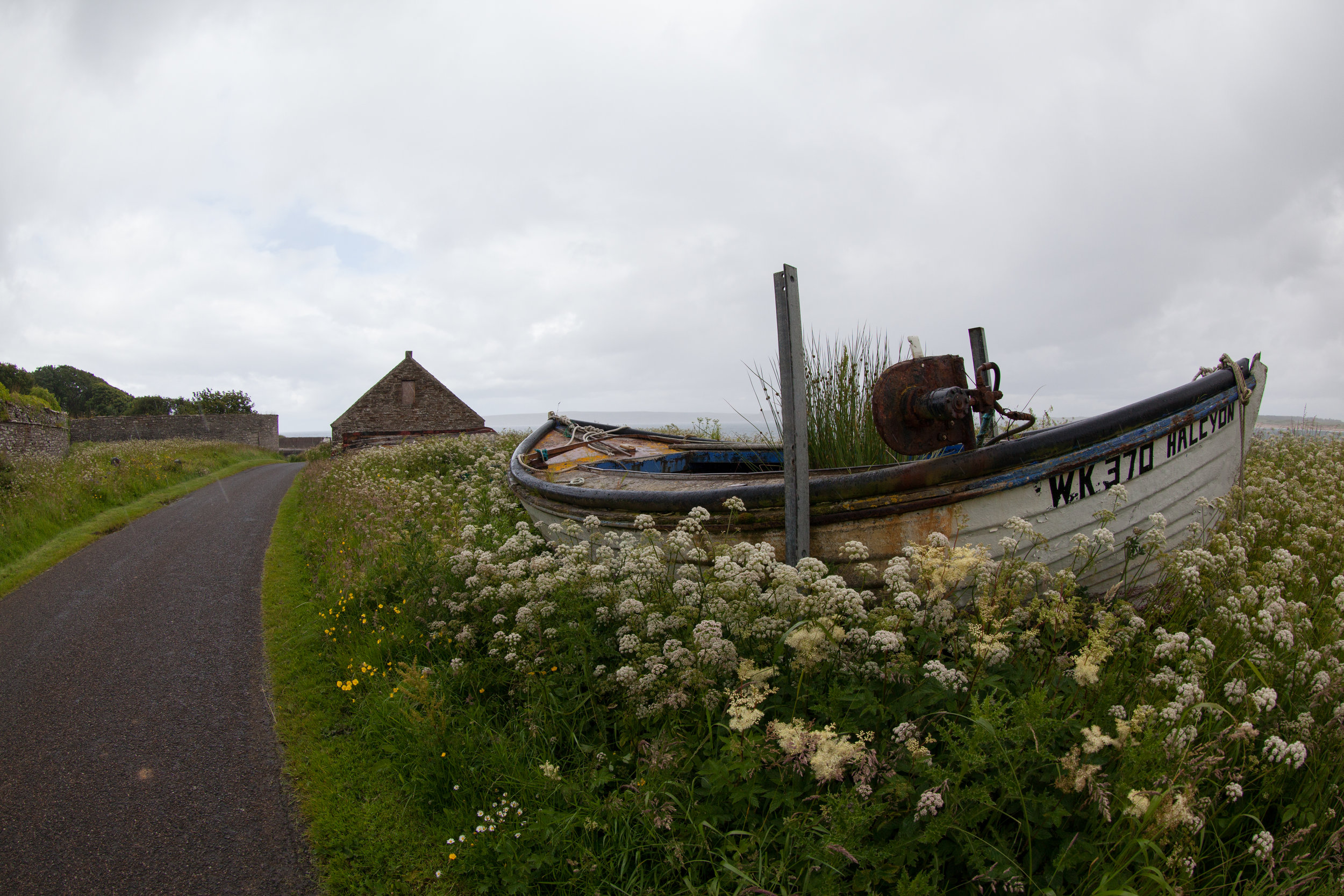 A boat lies in a meadow on the side of the road.