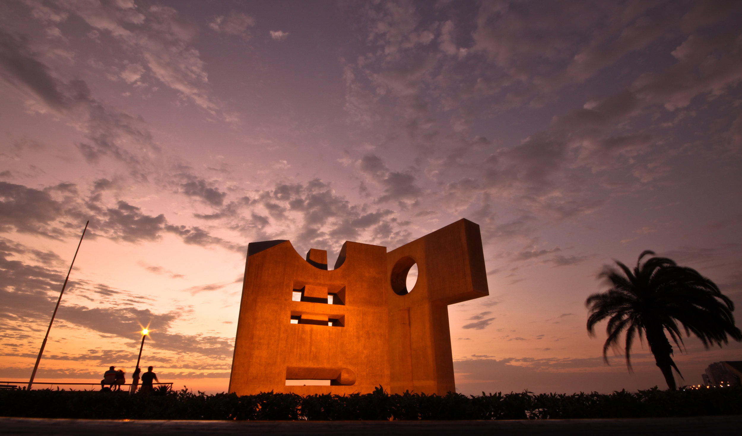 A vivid sun sets over some modern art on the malecon of Miraflores in Lima, Peru.