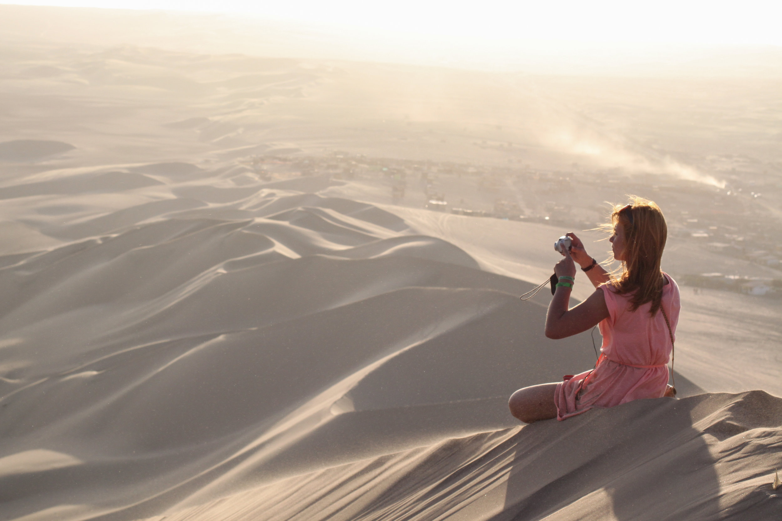 A red head girl sits on one of the largest sand dunes in South America to enjoy the sunset in Huacachina, Ica, Peru.
