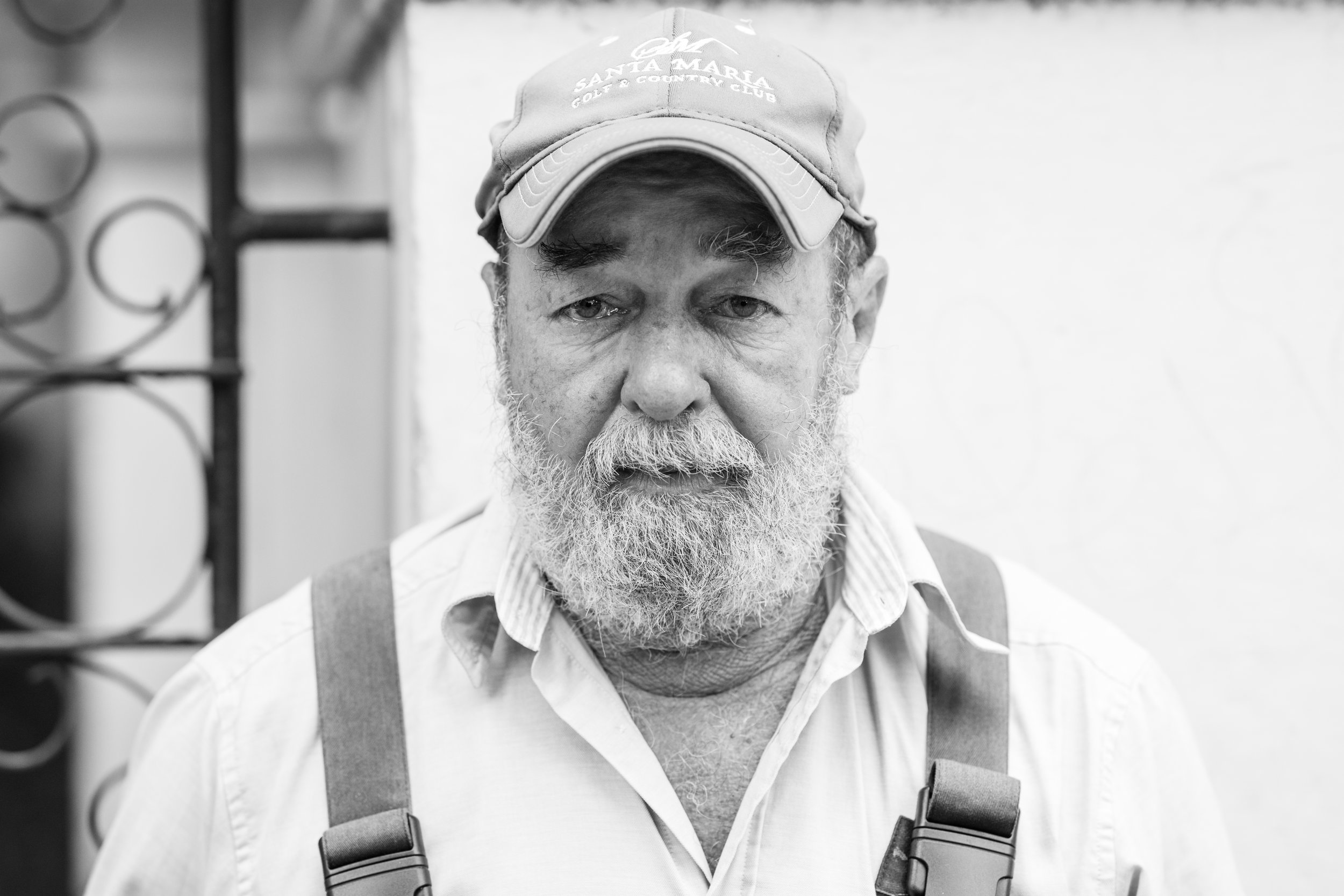 A black and white street portrait of a man in dungarees and cap in Havana, Cuba.