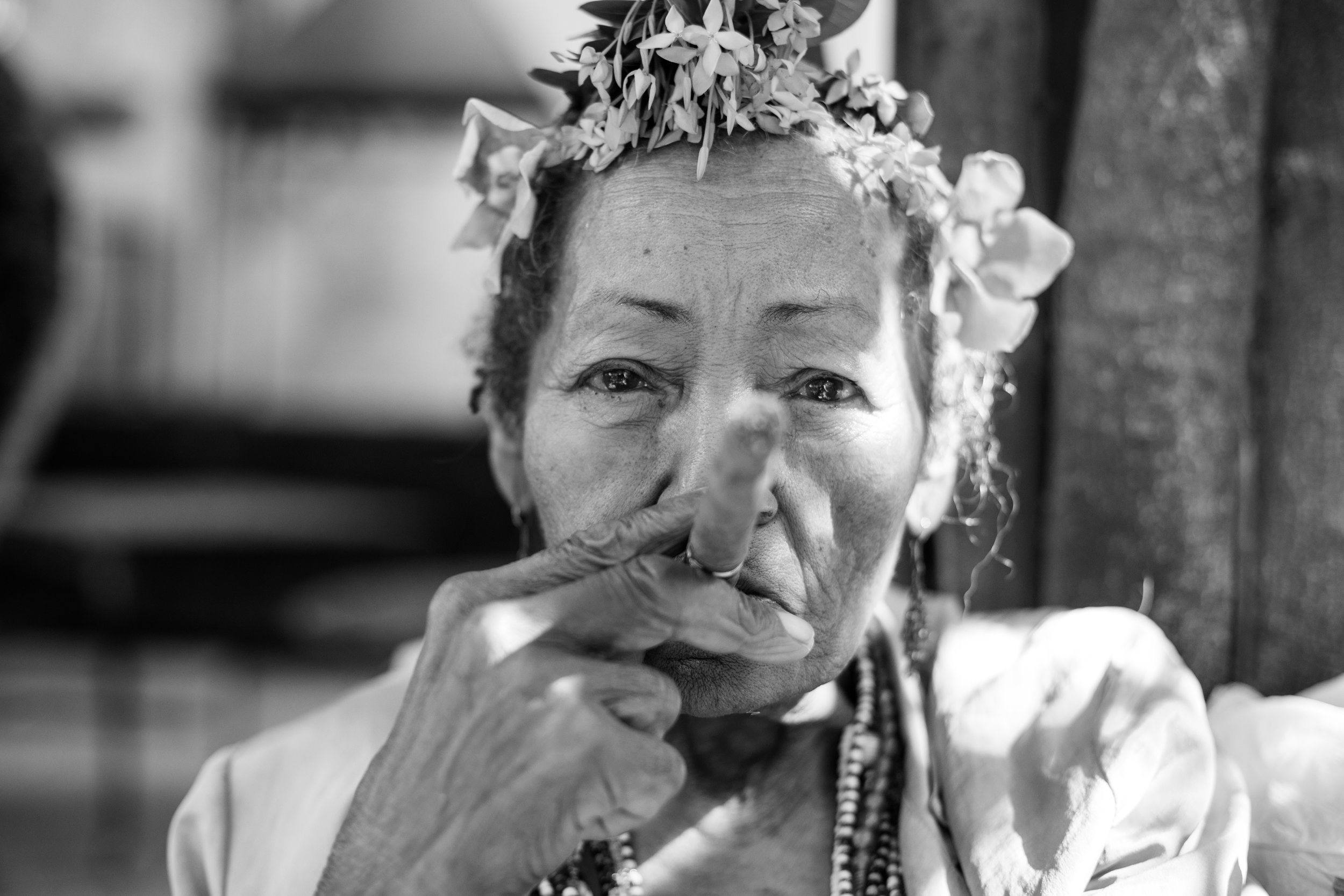 A black and white portrait of an elderly cuban lady with flowers in her hair and a large cuban cigar.