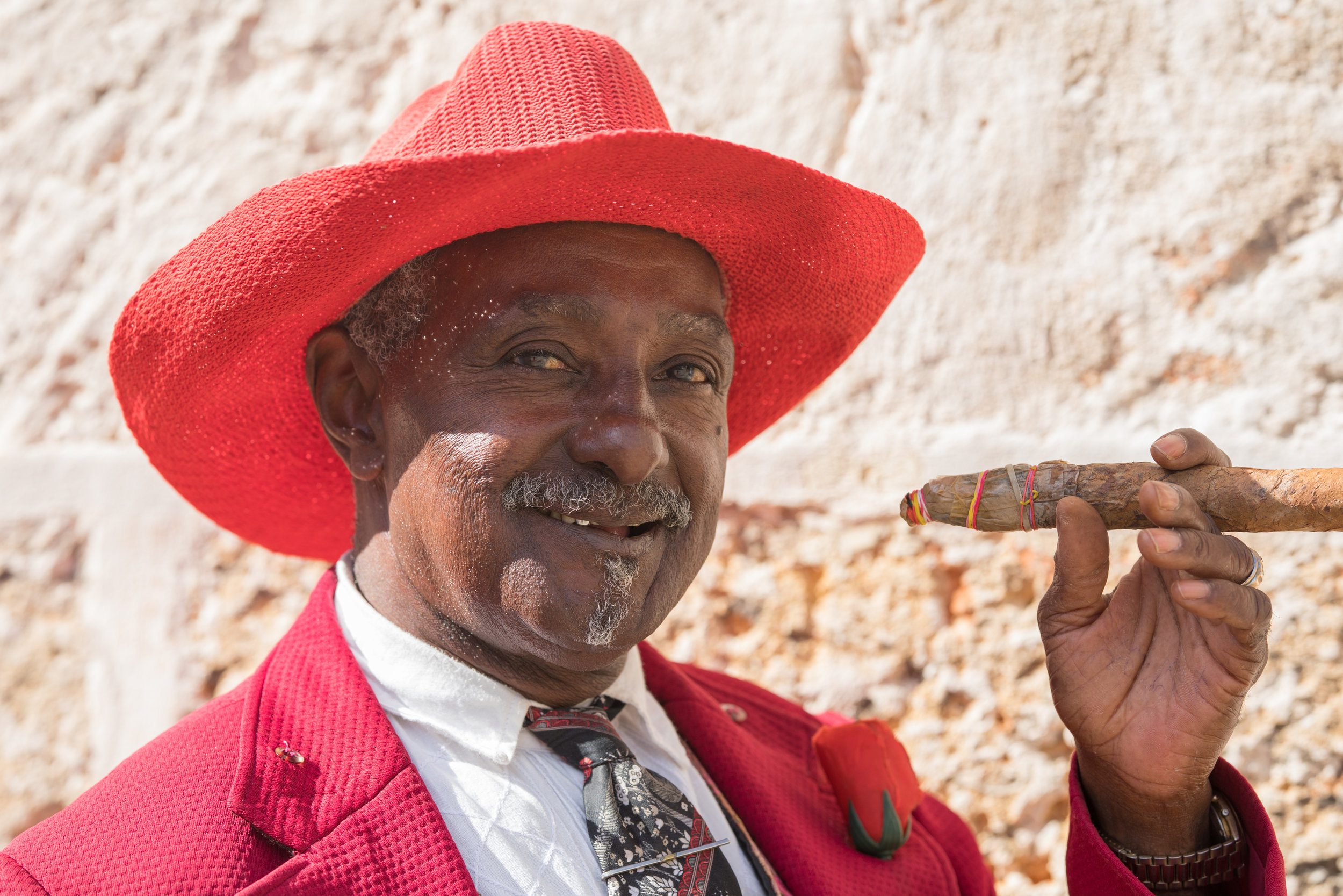 A friendly cuban in a bright red hat poses with a Cuban cigar.