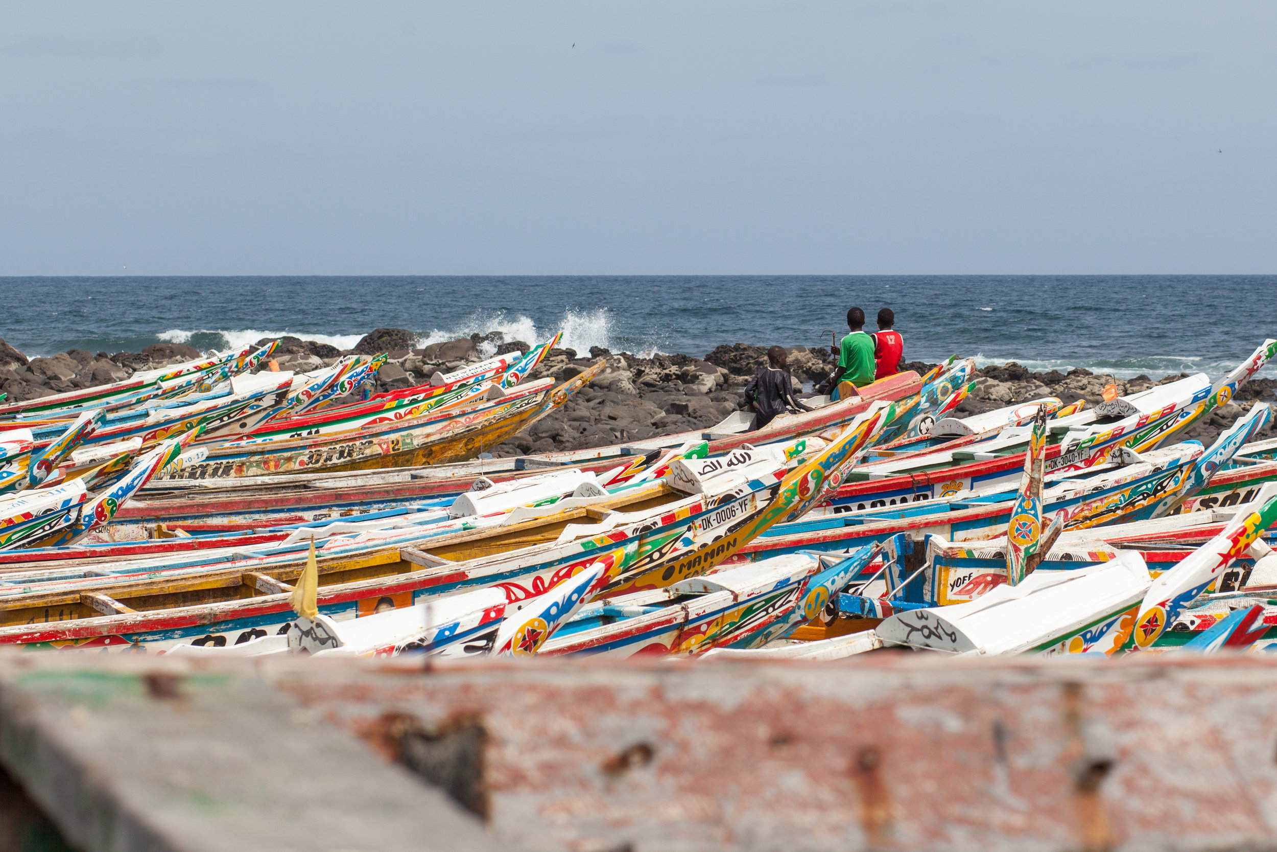 Children wearing football T-Shirts sit amongst the fishing boats at the far end of the beach at Yoff in Dakar.