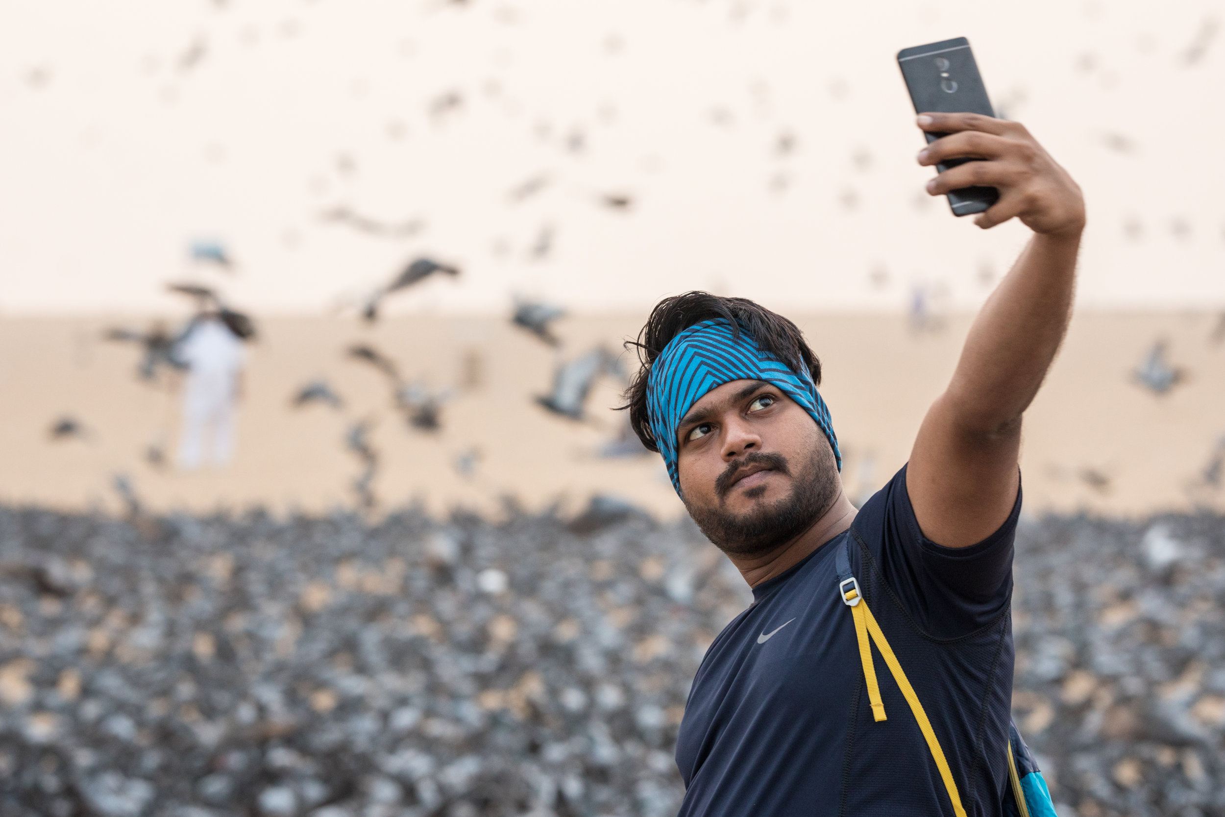 An Indian Man takes a selfie in front of feeding birds on the beach at Chennai.