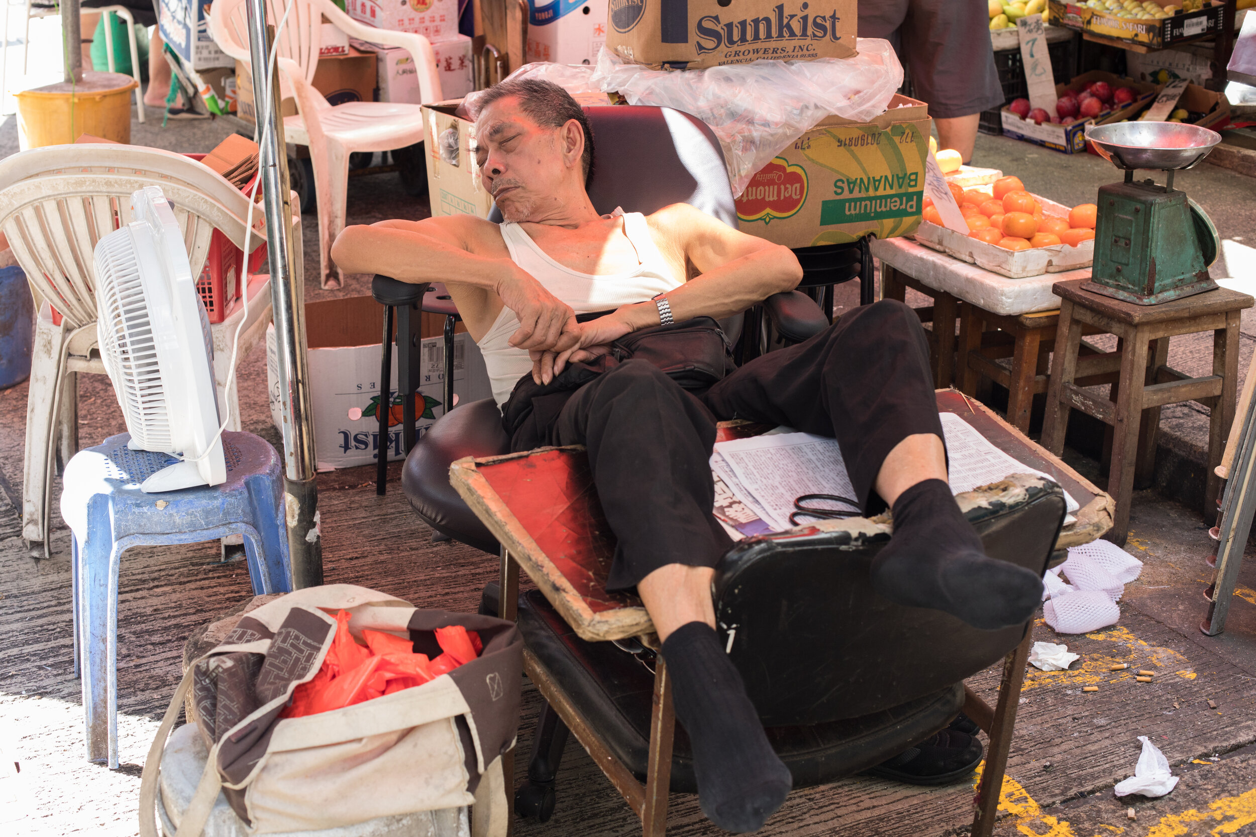 Street Portrait, a man rests on some chairs in a market in the centre of Hong Kong.