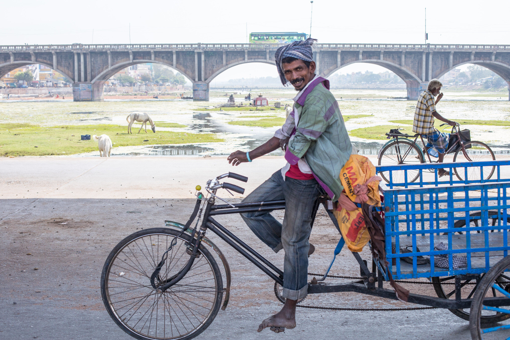 Two cyclists cross each other on a bridge across a river in Madurai, India.