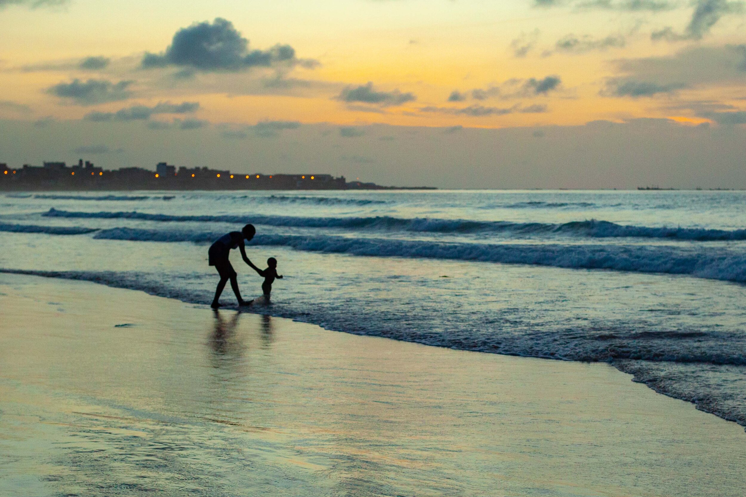 First steps, a silhouetted travel image of a Mother and her baby on the shore in West Africa.