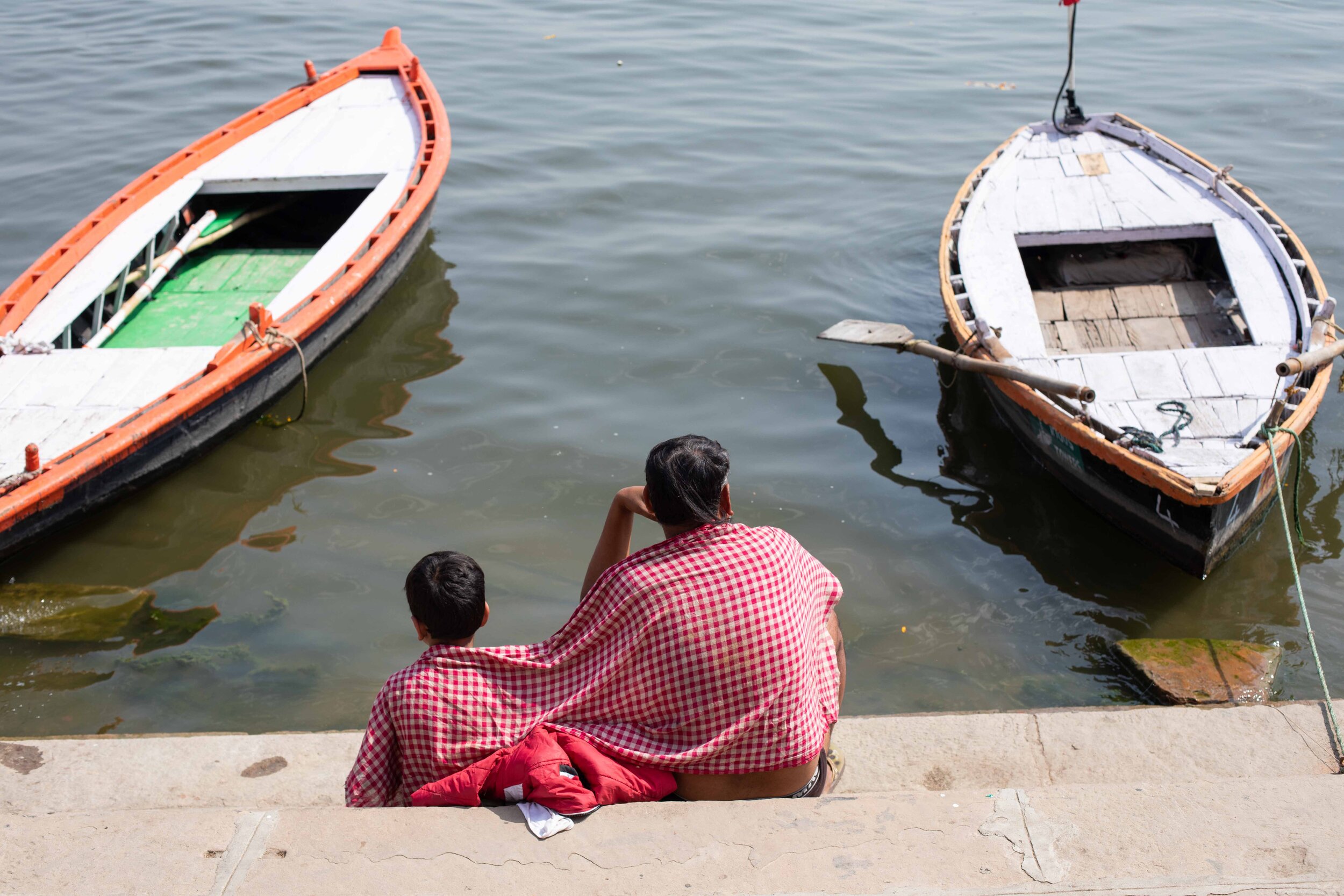 Father &amp; Son sit together on the edge of the River Gangs in Varanasi.