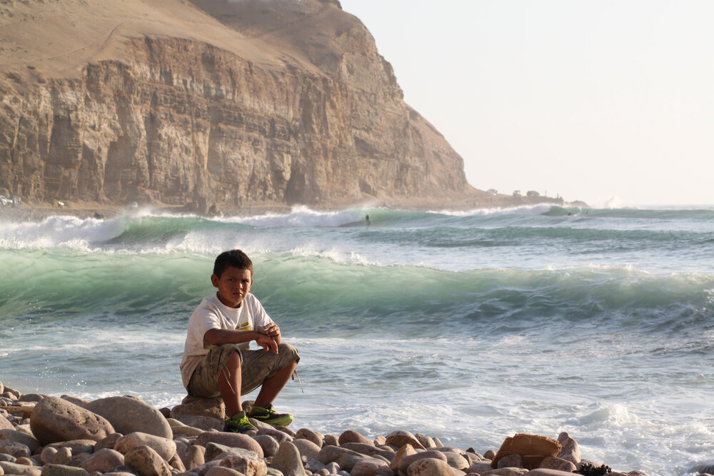 ·       Un niño sentado a la orilla del mar mientras se montan las olas a la distancia, La Herradura, Lima.