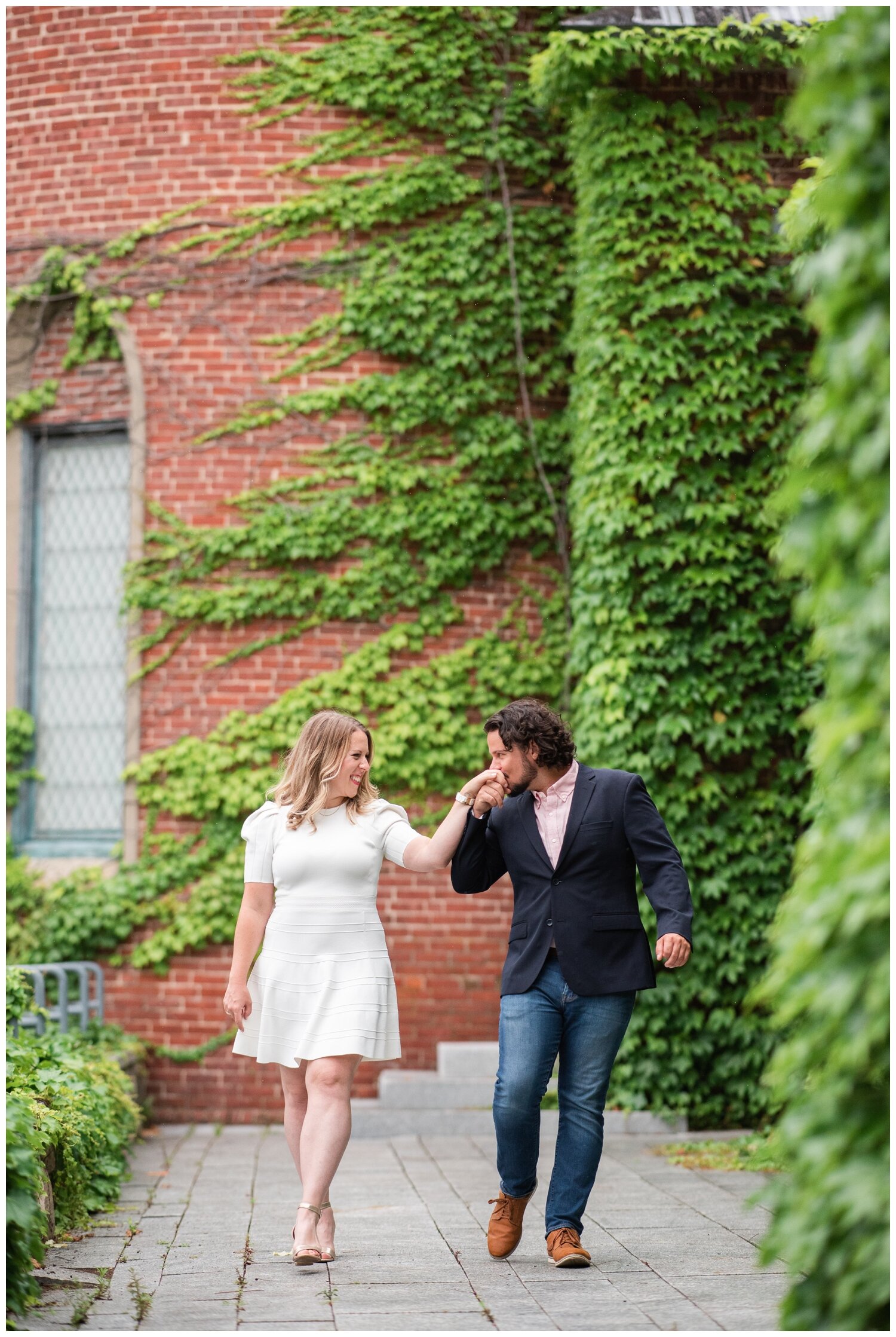 groom kissing bride's hand in front of ivy wall