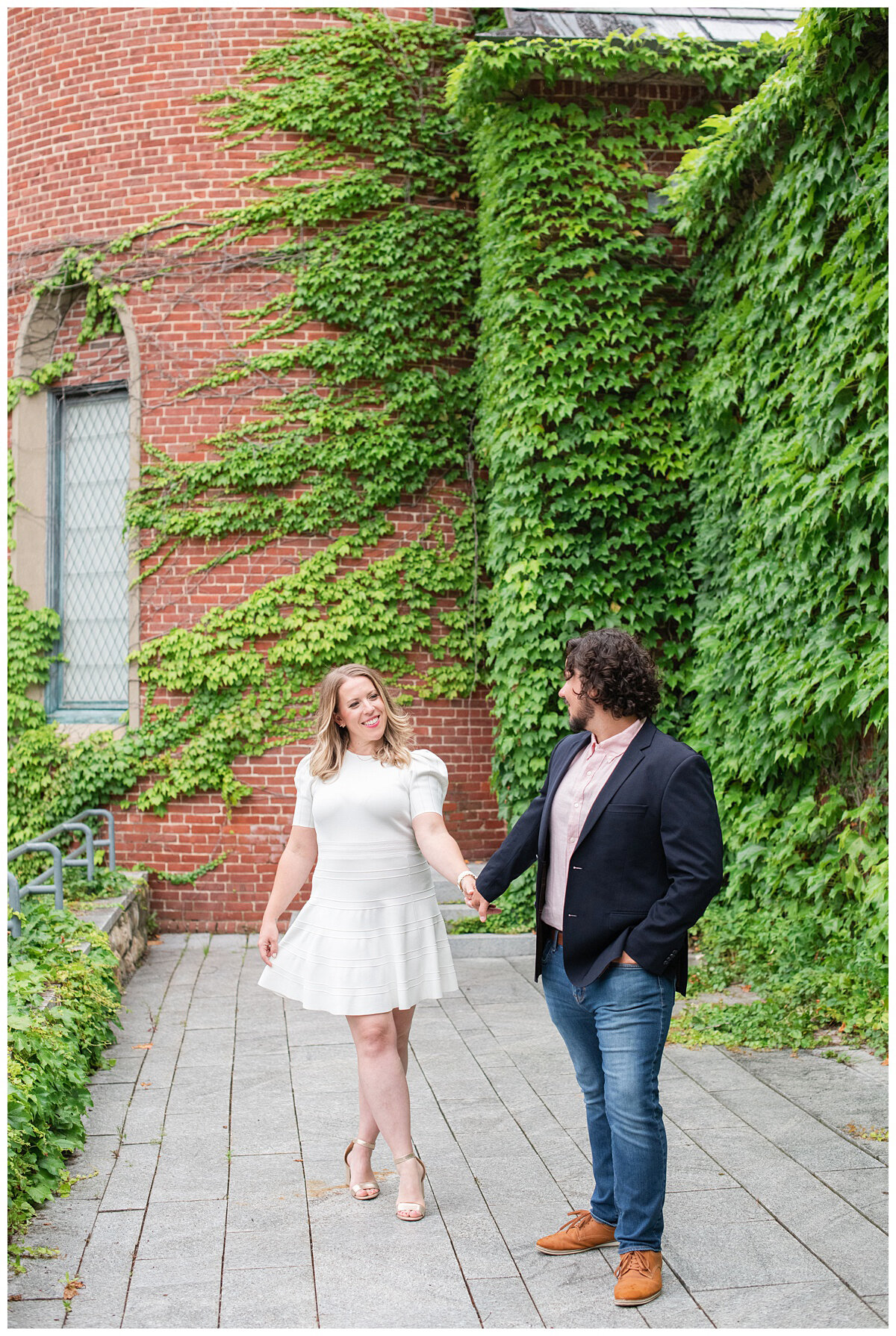 engaged couple walking in front of an ivy wall