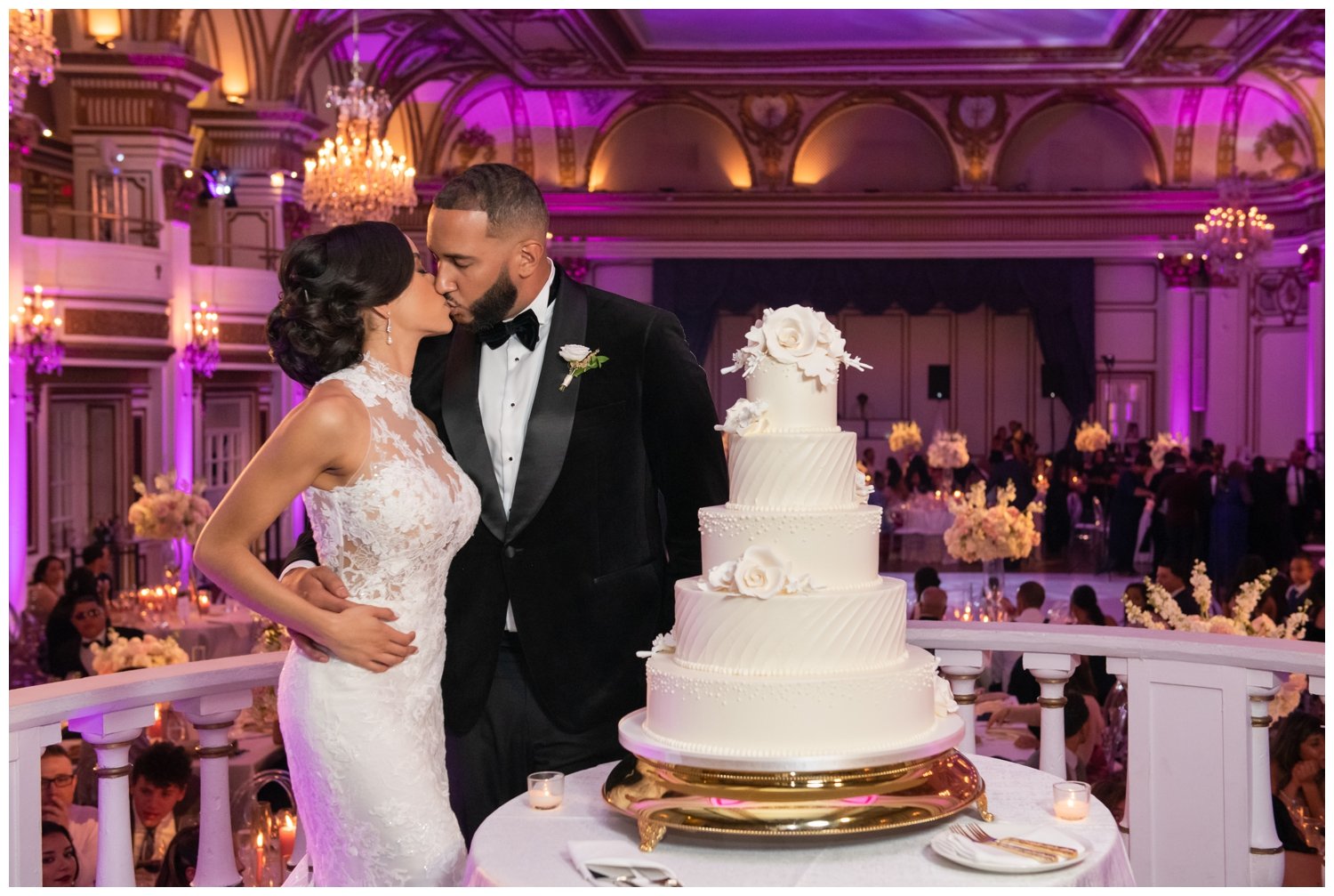 bride and groom kissing by five tier white wedding cake inside Fairmont Copley Plaza Hotel