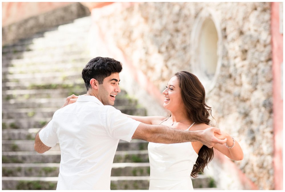 engaged couple wearing white dancing on steps at Vizcaya Museum engagement photos